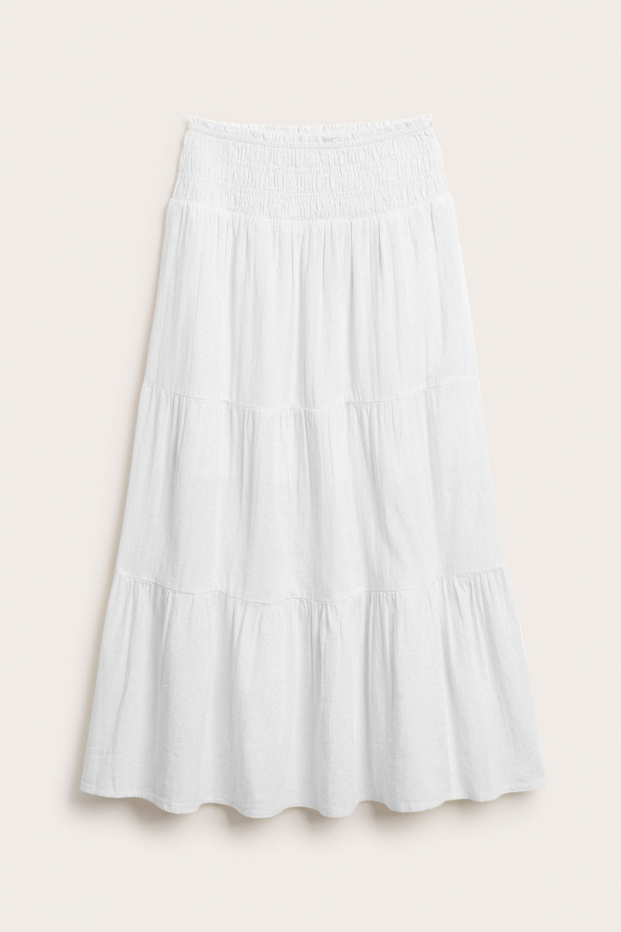 Frontvy av en vit, mjuk vävd bomullsmaxikjol med smockad midja och volanger.
