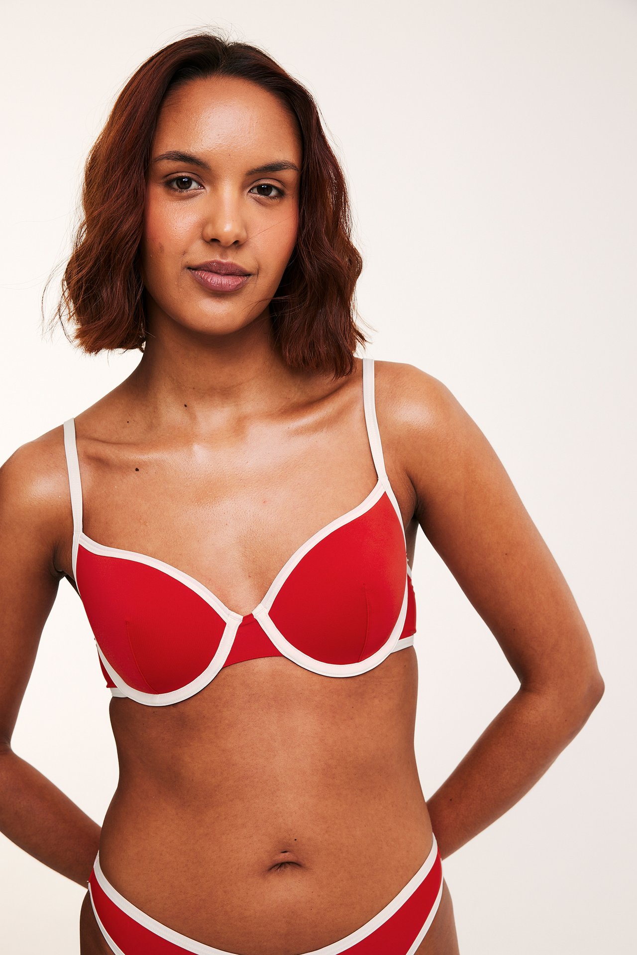 Framifrån: Kvinna bär röd bygel-bikini-bh med vit kant och matchande bikinibotten.