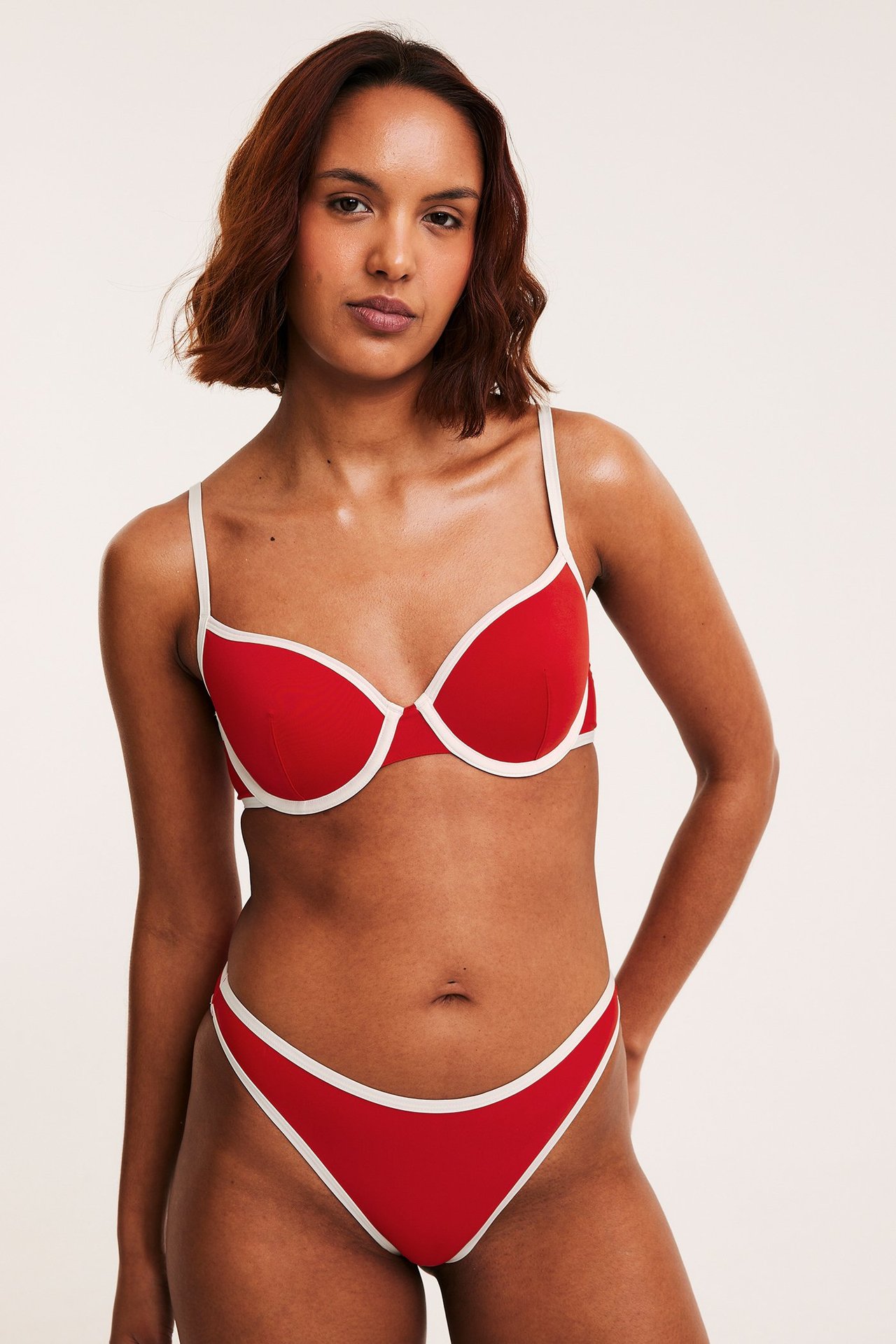 Framifrån: Kvinna i röd bikini-bh med vit kant och matchande bikini-trosa.