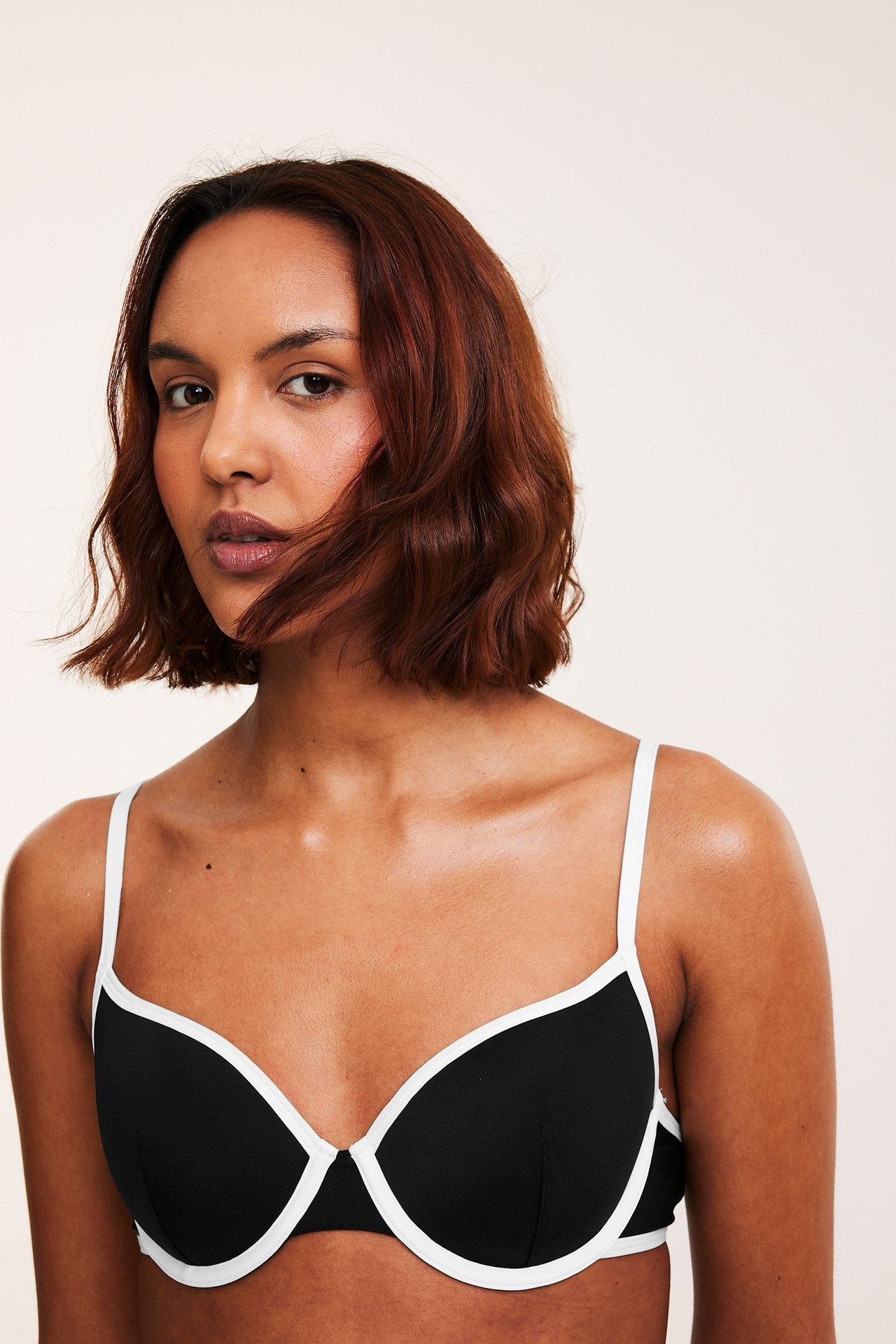 Lähikuva edestä naisesta, jolla on musta bikiniliivi valkoisilla reunuksilla ja kapeilla valkoisilla olkaimilla.