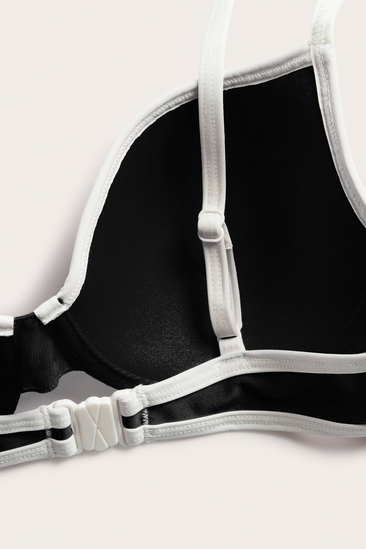 Widok z tyłu z bliska czarnego biustonosza bikini z białą lamówką, regulowanymi ramiączkami i białym plastikowym zapięciem.