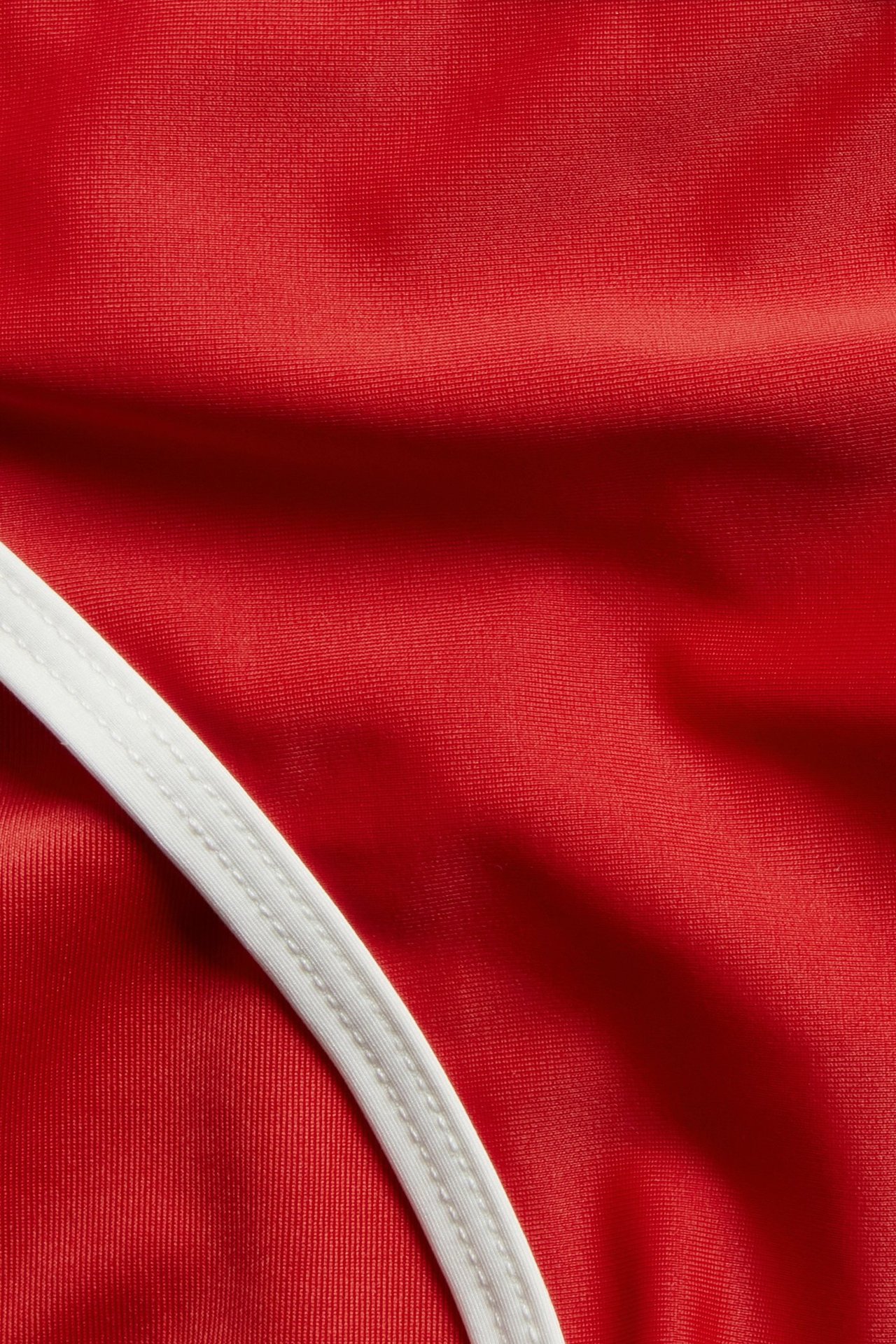 Nærbilde av ensfarget rødt bikinitrusestoff med en sydd hvit kant.