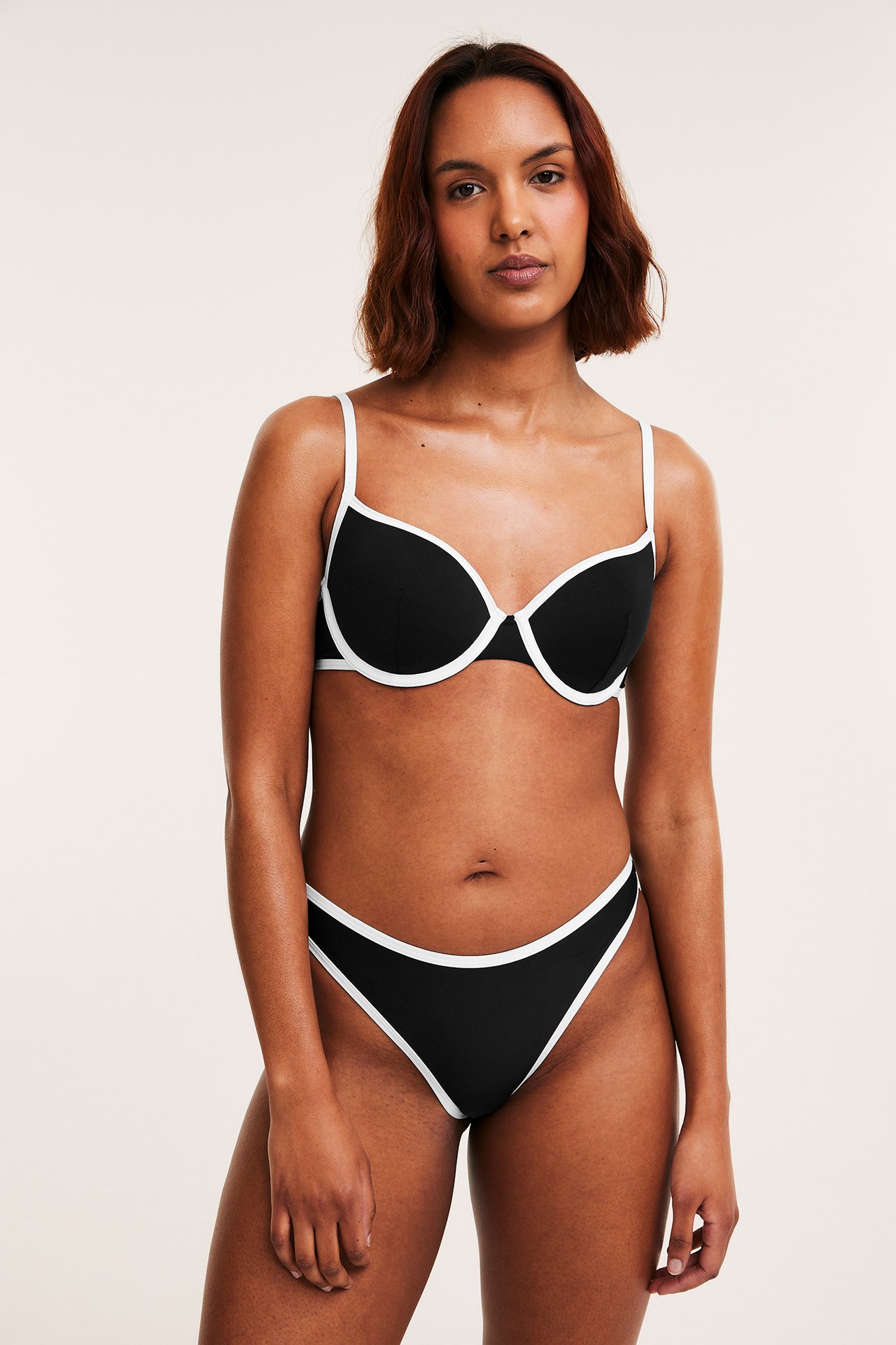 Framifrån, en kvinna bär svarta brazilian bikinitrosor och matchande bikini-bh, båda med vit kant.