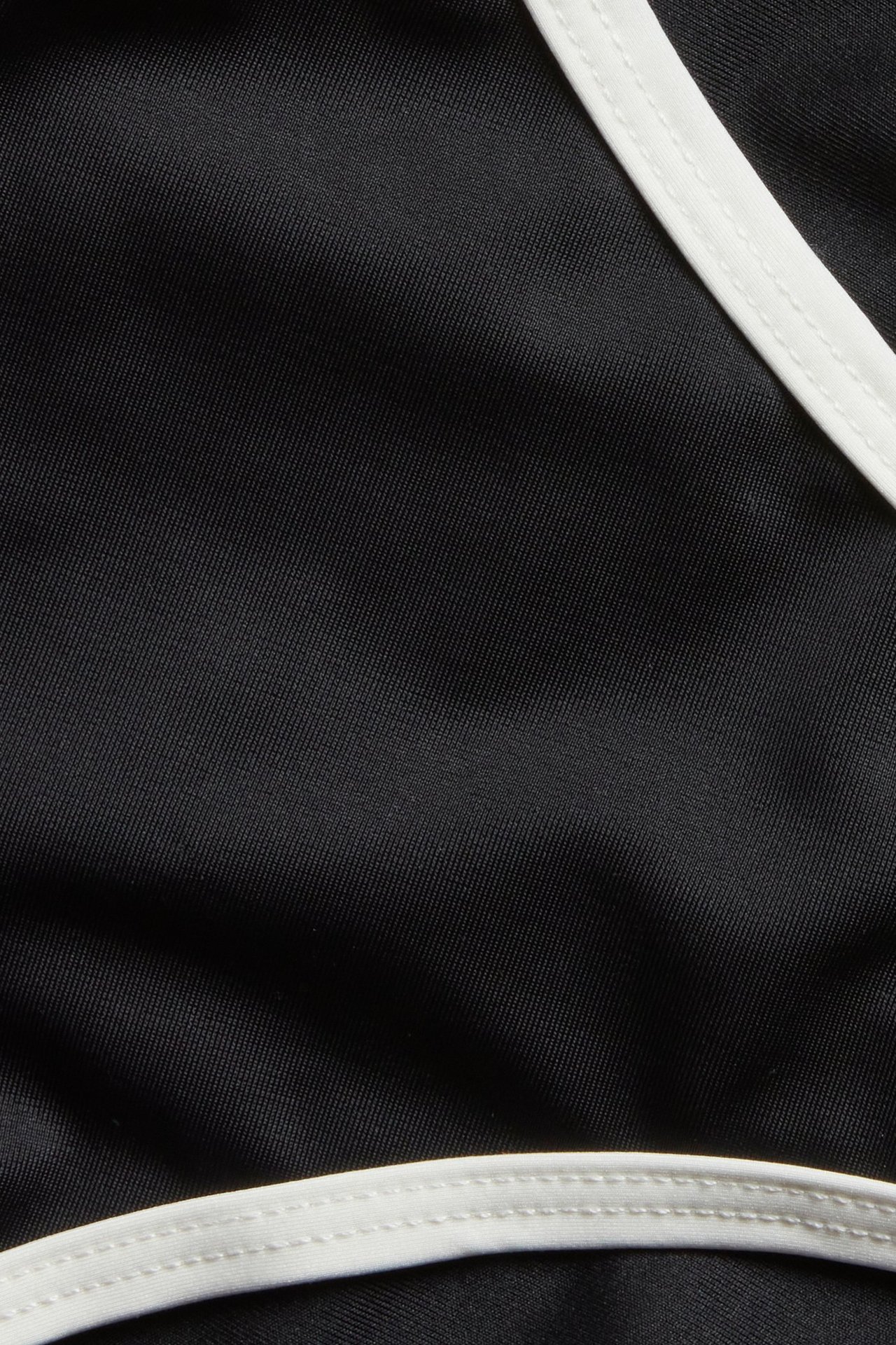 Nærbilde av en svart brazilian bikinitruse med hvite kantdetaljer.