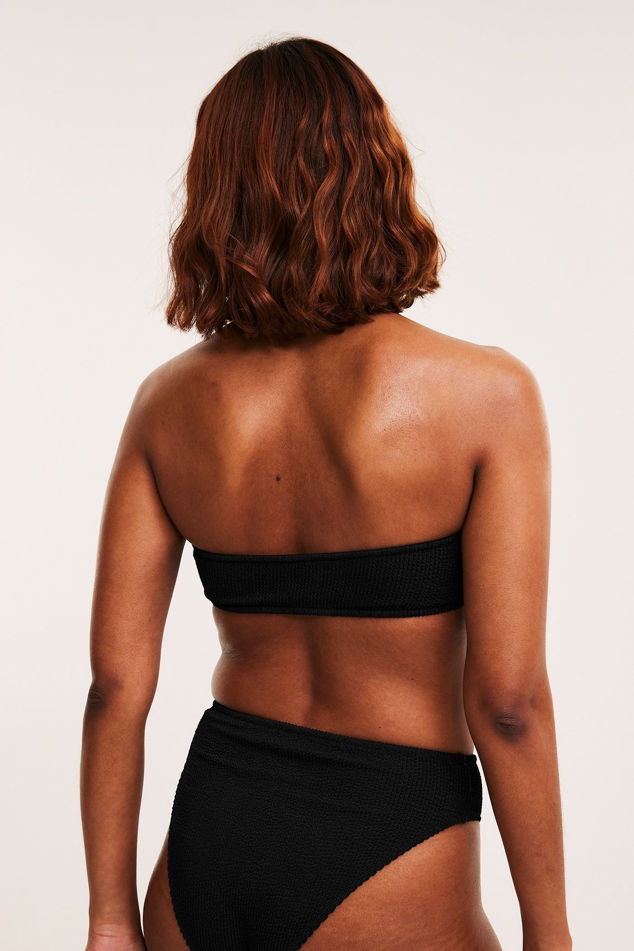 Naisen takakuva, yllään musta kuvioitu bandeau-bikinin yläosa ja yhteensopivat bikinin alaosat.