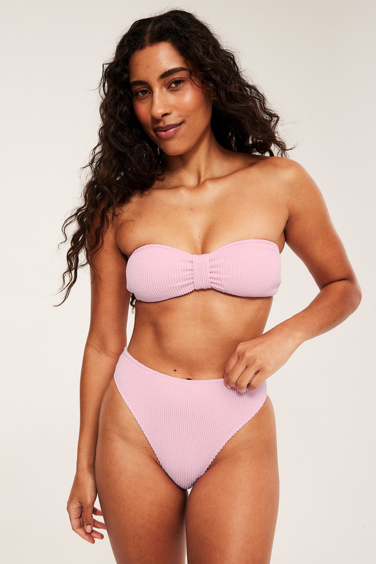 Edestäpäin: nainen pinkissä kuvioidussa bandeau-bikinitopissa ja yhteensopivissa korkeissa bikinialaosissa.