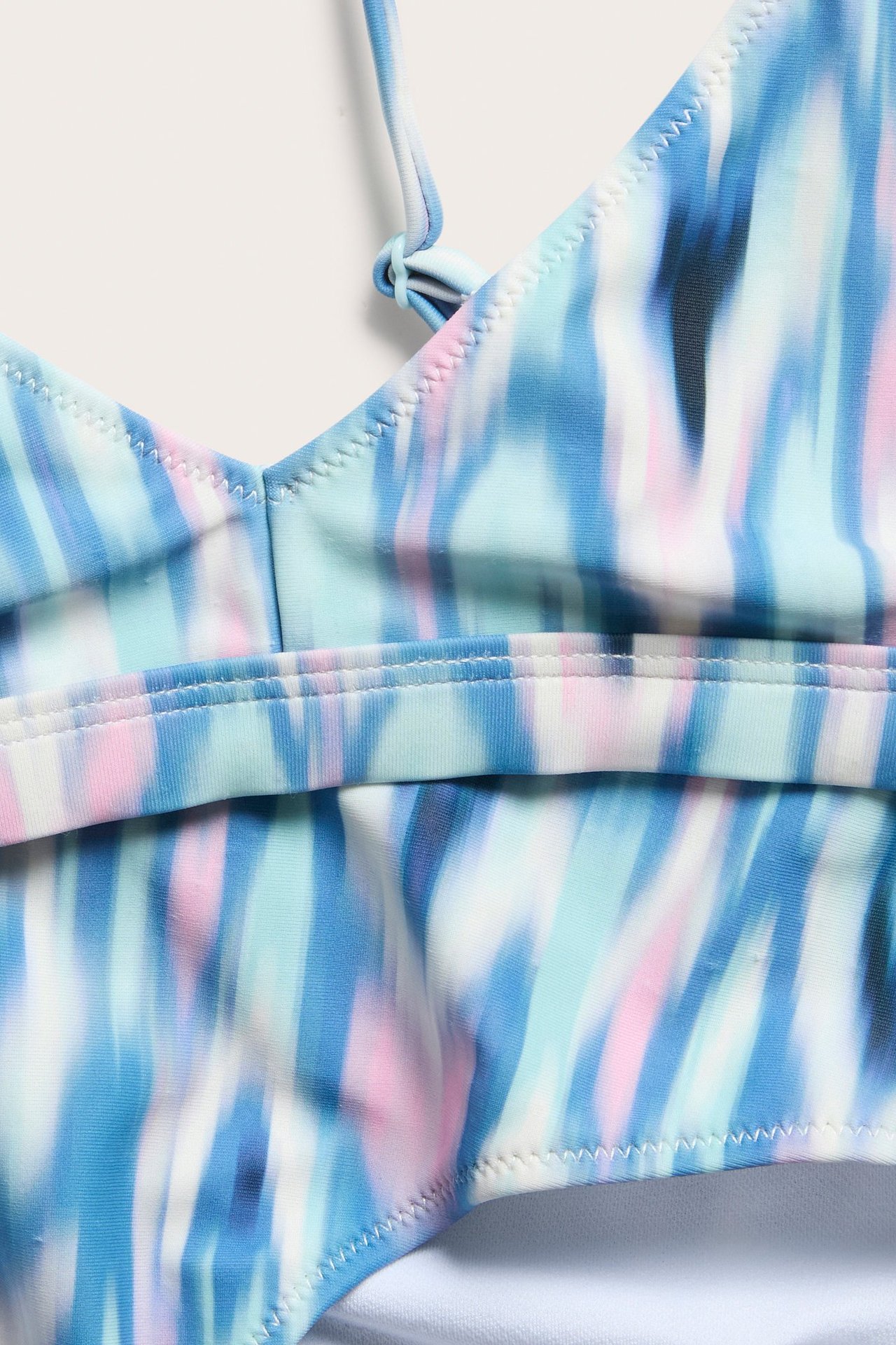 Zbliżenie na jasno turkusowy biustonosz bikini trójkątny z niebieskim, różowym i białym abstrakcyjnym wzorem.