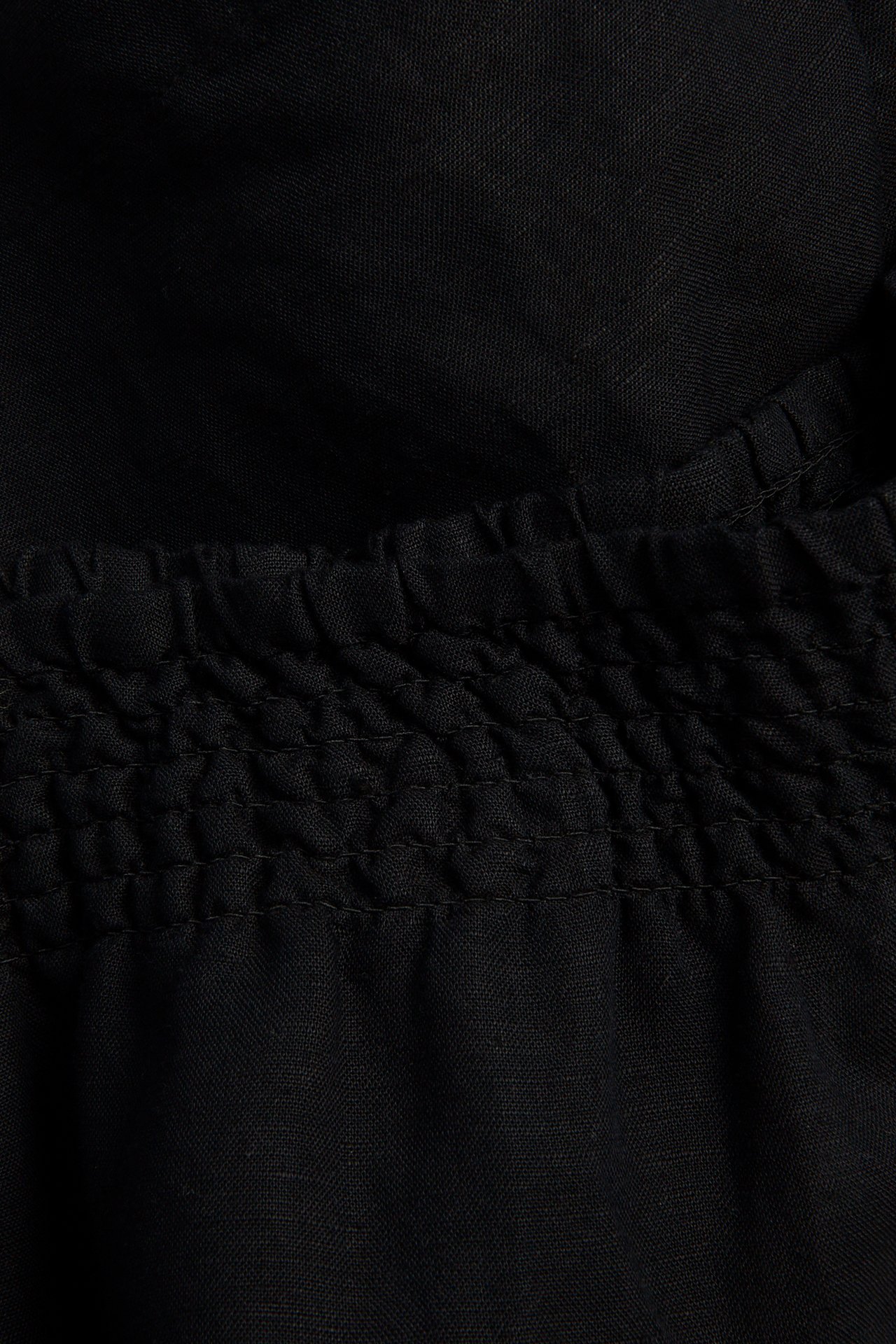 Nærbilde av sorte shorts i viskose- og linblanding med smockelastikk i midjen.