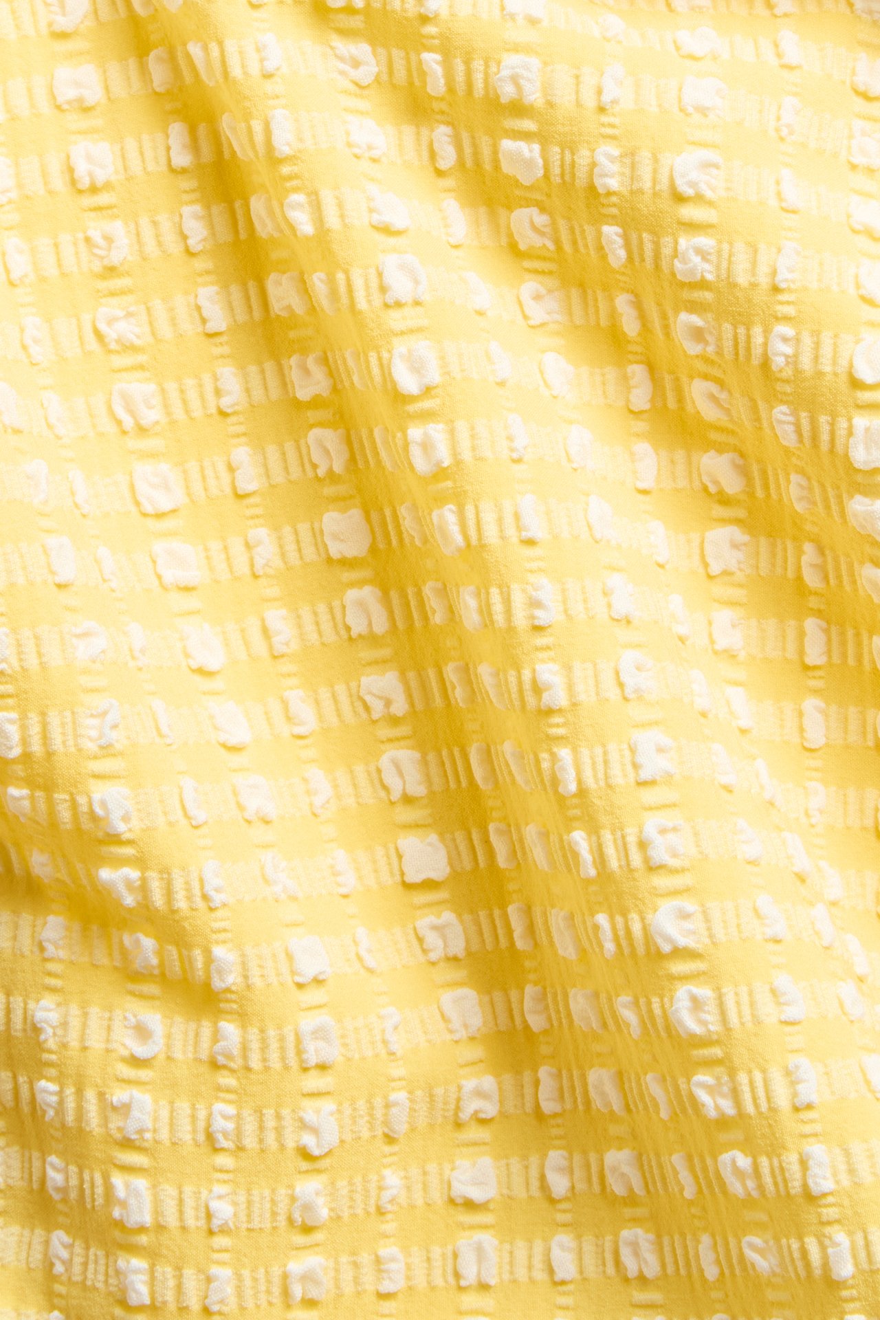 Lähikuva keltaisesta ja valkoisesta kuvioidusta ruudullisesta bikinialahousukankaasta.