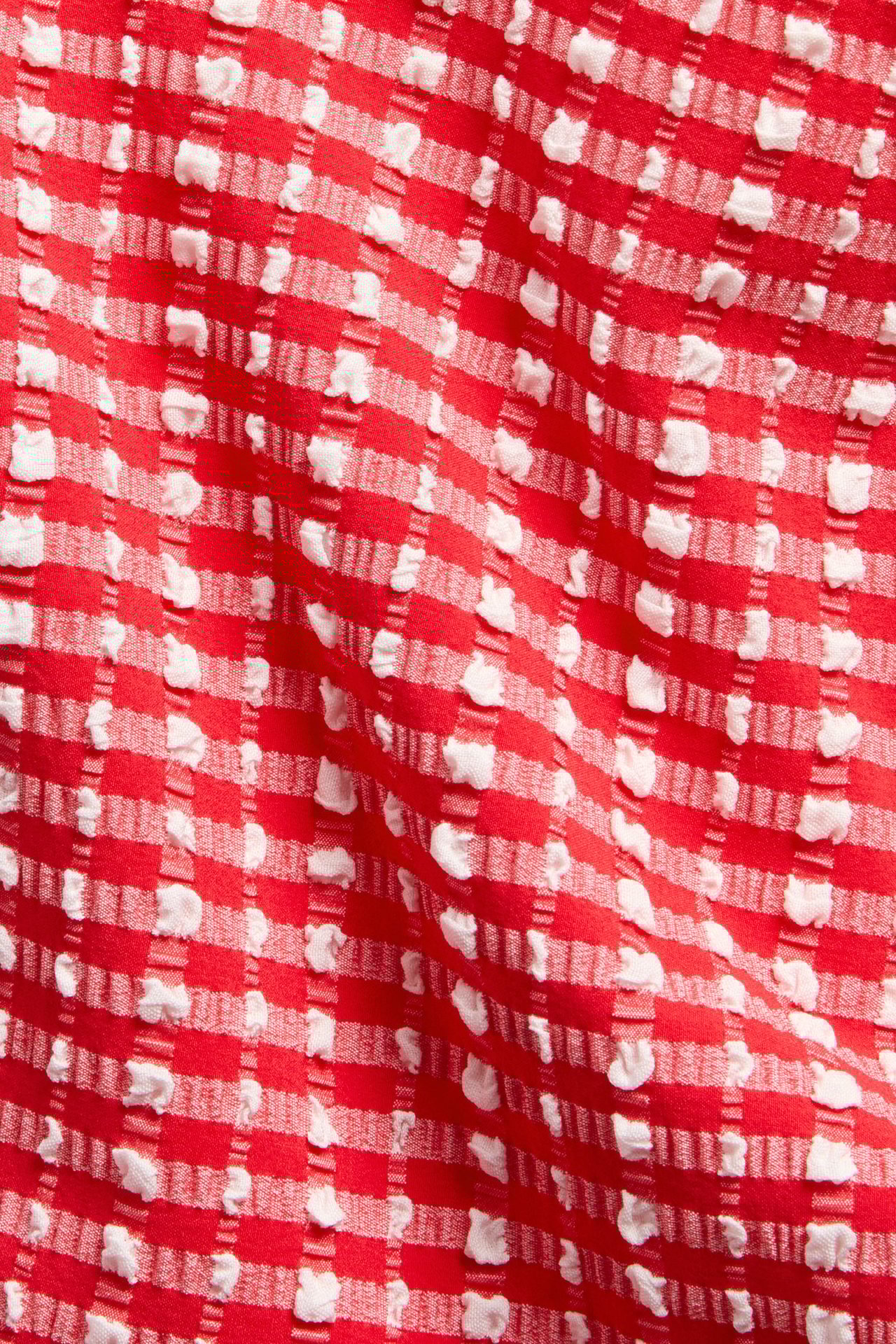 Lähikuva punavalkoisesta ruudullisesta bikinialahousukankaasta, jossa on kuvioitu, ryppyinen pinta.