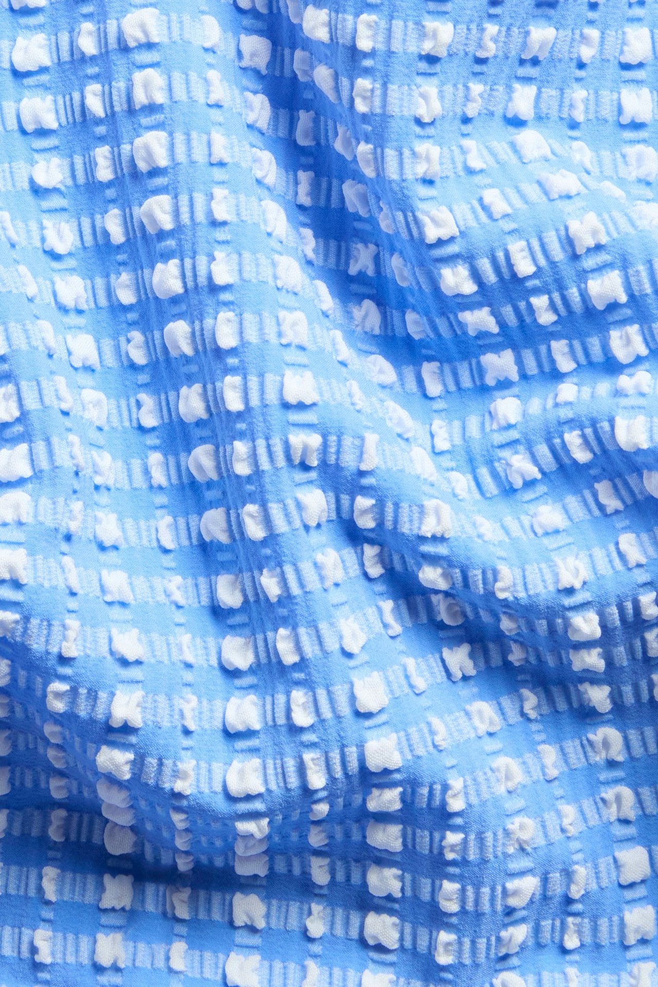 Lähikuva sinivalkoisesta, teksturoidusta ruudullisesta bikinialaosakankaasta.