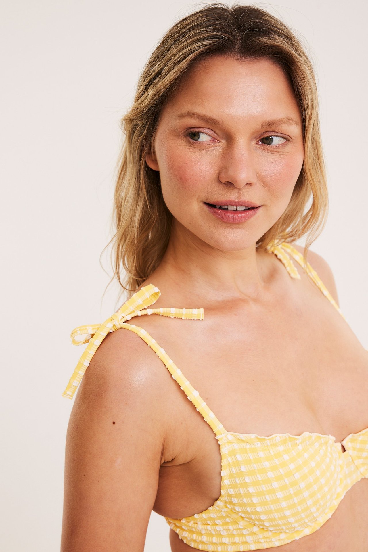 Lähikuva naisesta, jolla on keltainen ja valkoinen ruudullinen bikinin yläosa solmittavilla olkaimilla.