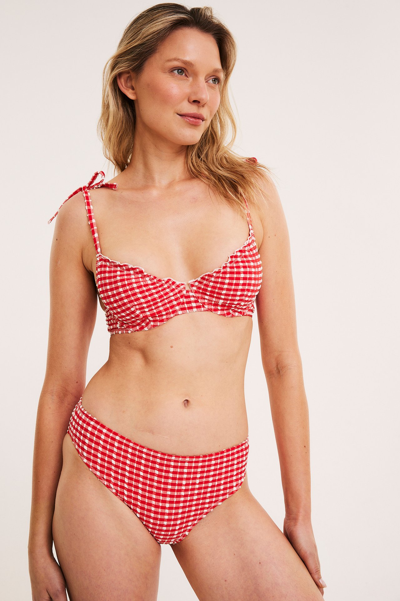Edestä: nainen yllään punavalkoruudullinen toppimaton bikiniyläosa solmittavilla olkaimilla ja alaosat.
