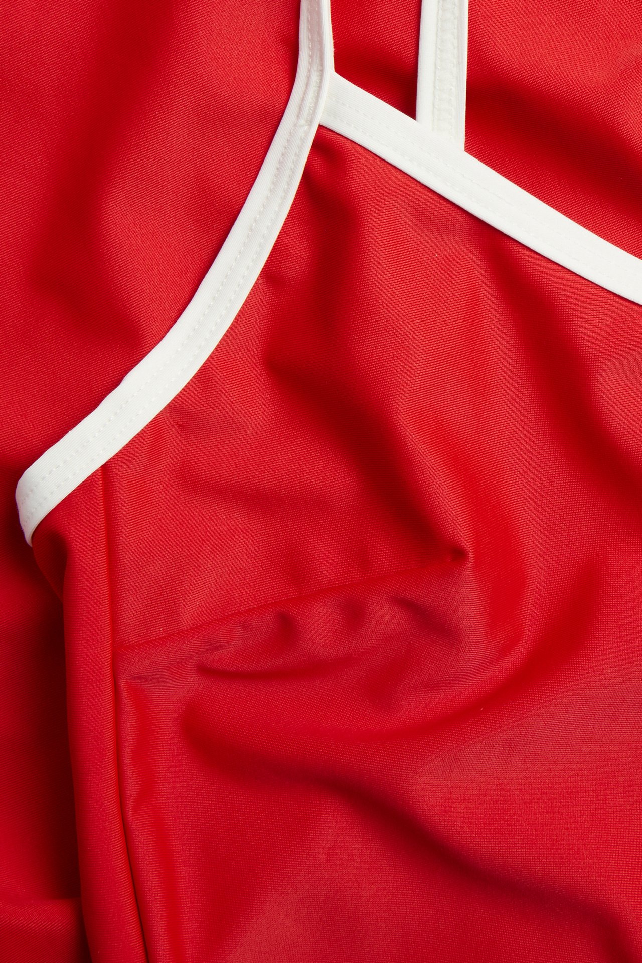 Närbild av en röd baddräkt med vita kontrasterande kantband vid axelband och halsringning.