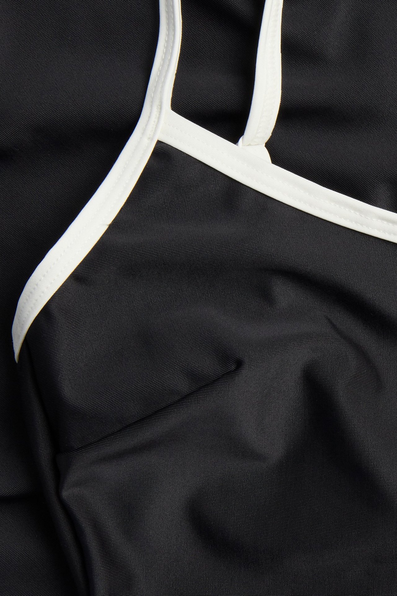 Zbliżenie czarnego stroju kąpielowego z białymi, kontrastowymi lamówkami wzdłuż dekoltu i ramiączek.