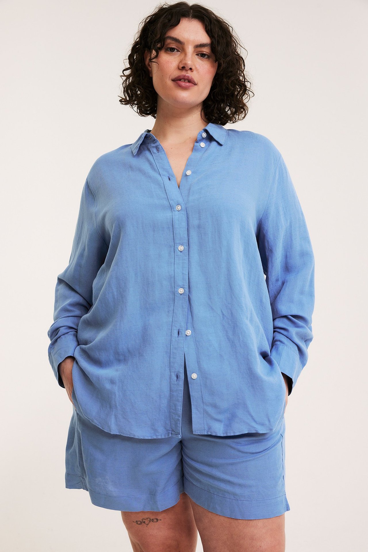 Frontbilde av kvinne i blå linstoffshorts med smocksøm i midjen og en matchende skjorte.