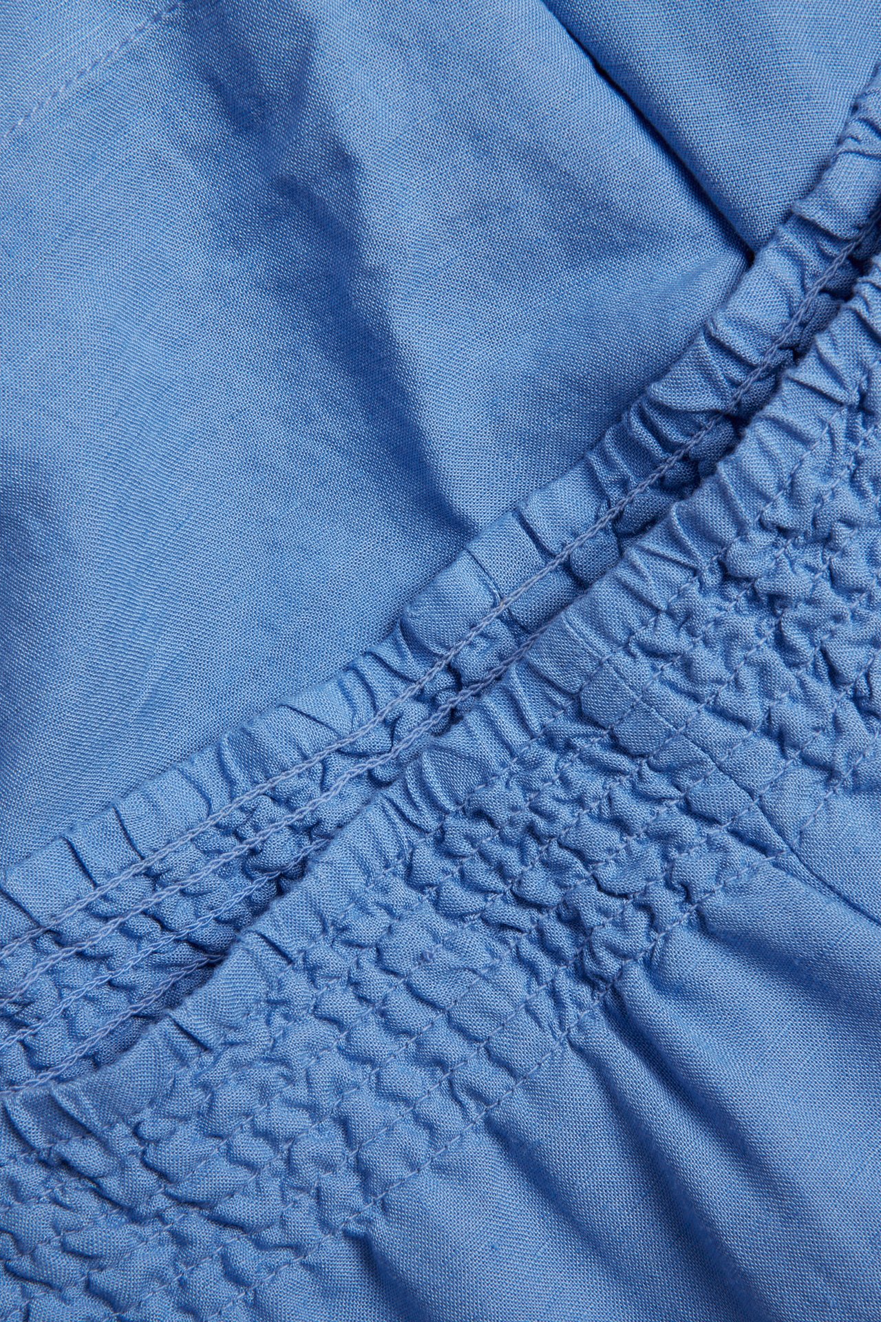 Nærbilde av blå shorts i viskose- og linstoff med smock-elastikk i midjen.