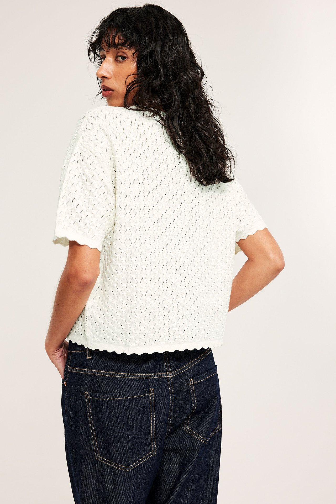 Bakre sidovy av en kvinna i en offwhite mönsterstickad kortärmad tröja med mörkblå jeans.