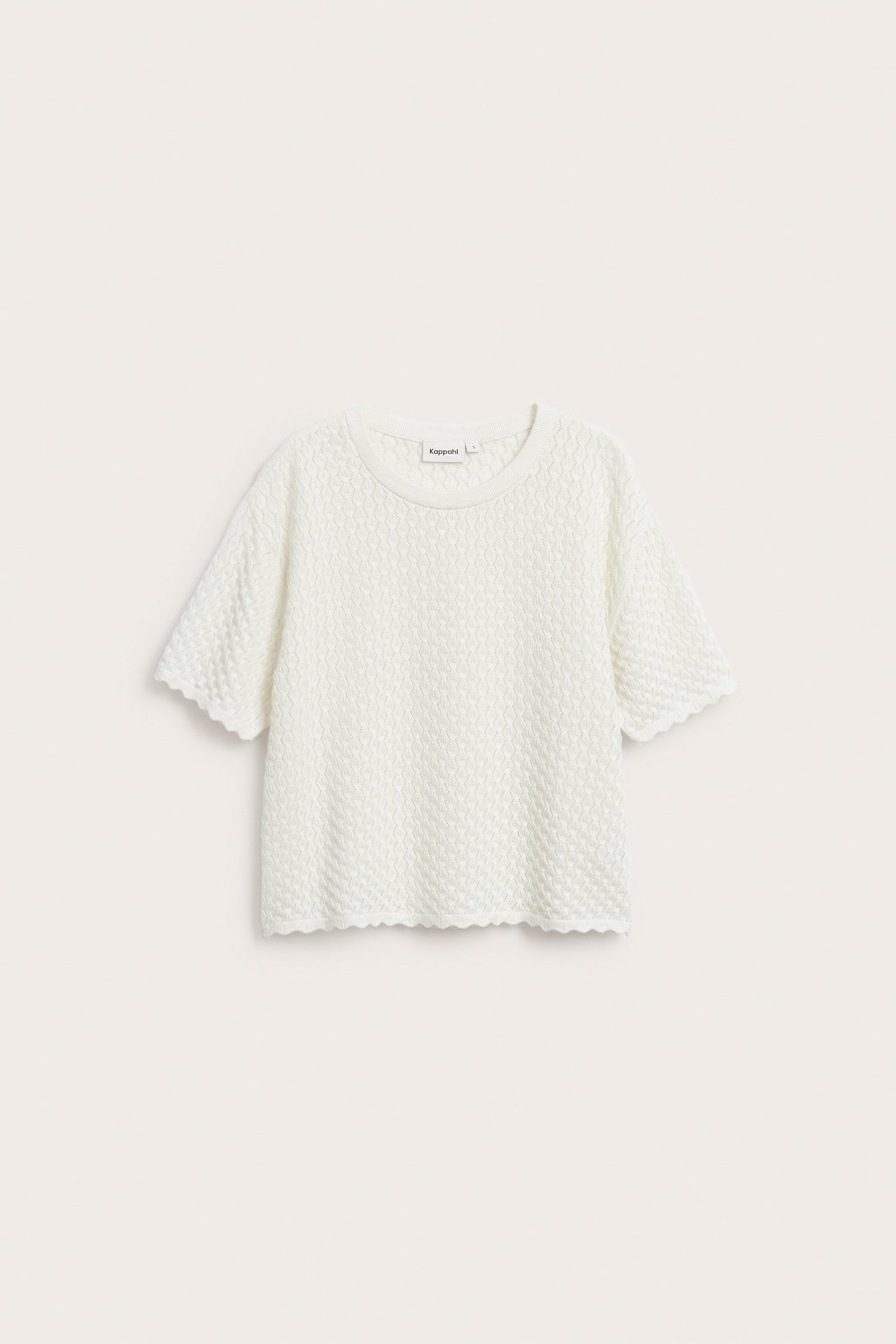 Edestä, luonnonvalkoinen kuviollinen lyhythihainen puuvillaneule, jossa on aaltoilevat reunat.