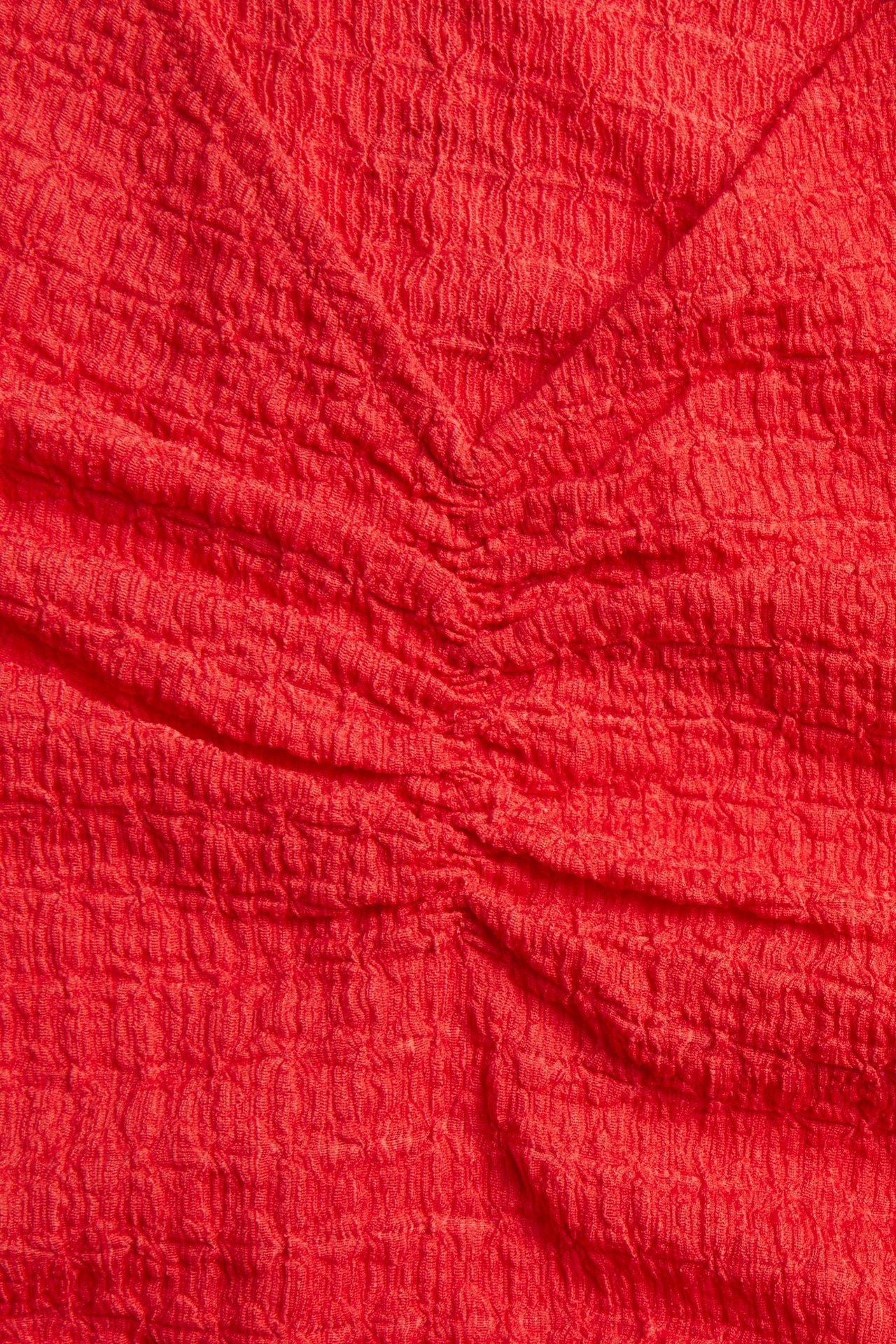 Zbliżenie czerwonego, strukturalnego topu z marszczeniami przy dekolcie w kształcie litery V.
