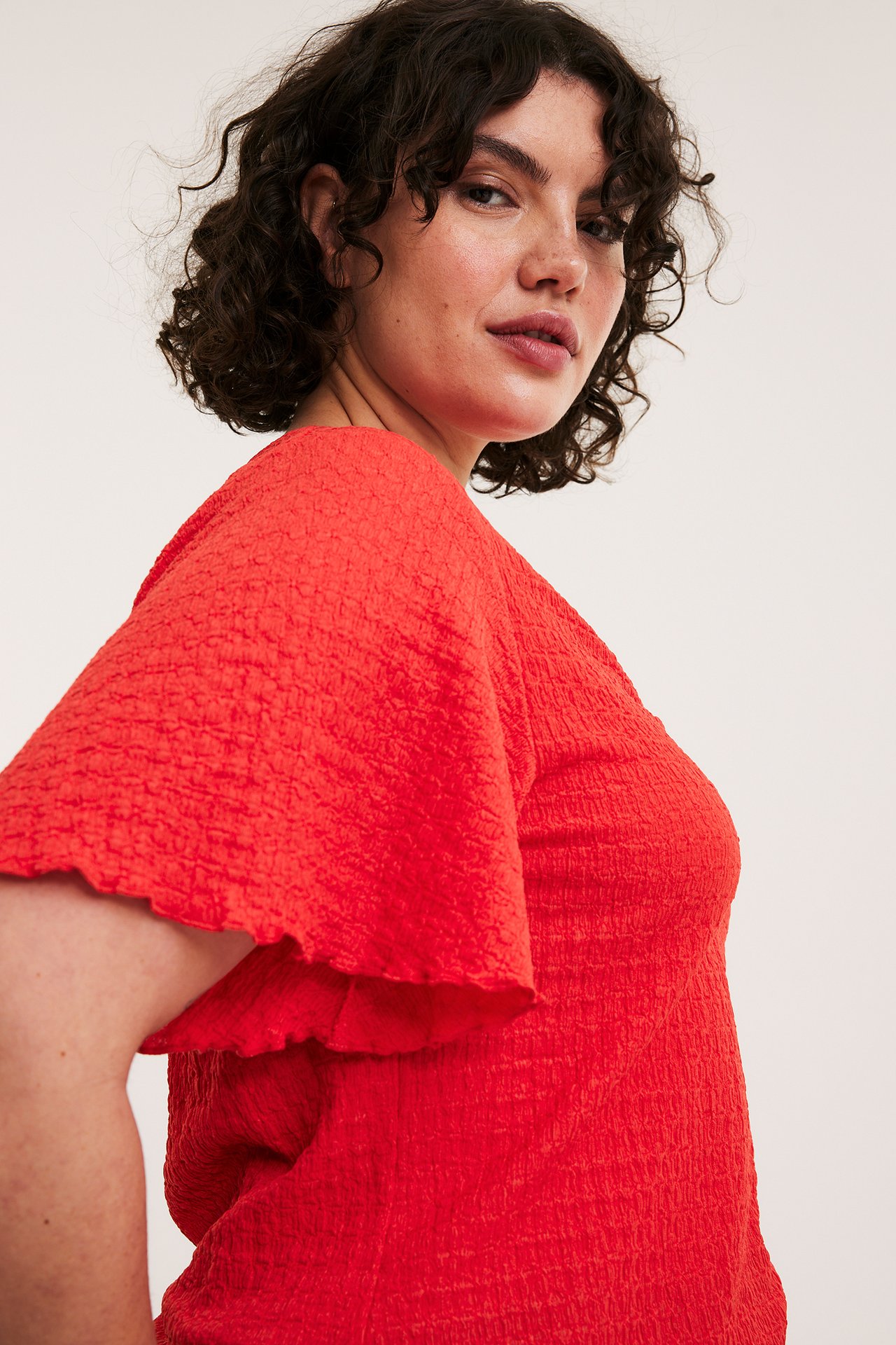 Lähikuva naisesta, joka käyttää punaista teksturoitua lyhythihaista toppia, jossa on röyhelöhihat.