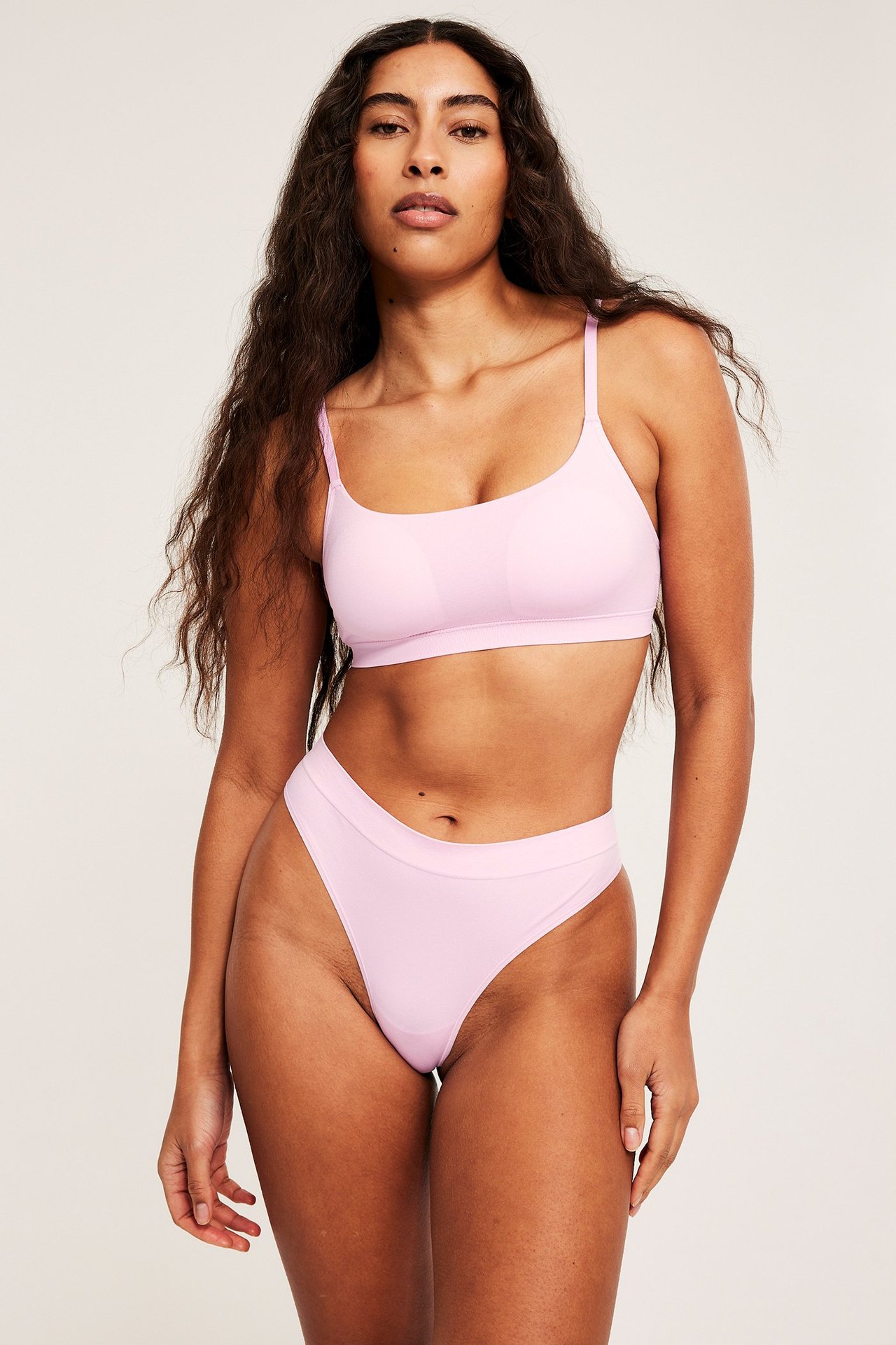Forfra, kvinne iført en sømløs rosa stringtruse og en matchende sømløs rosa BH.