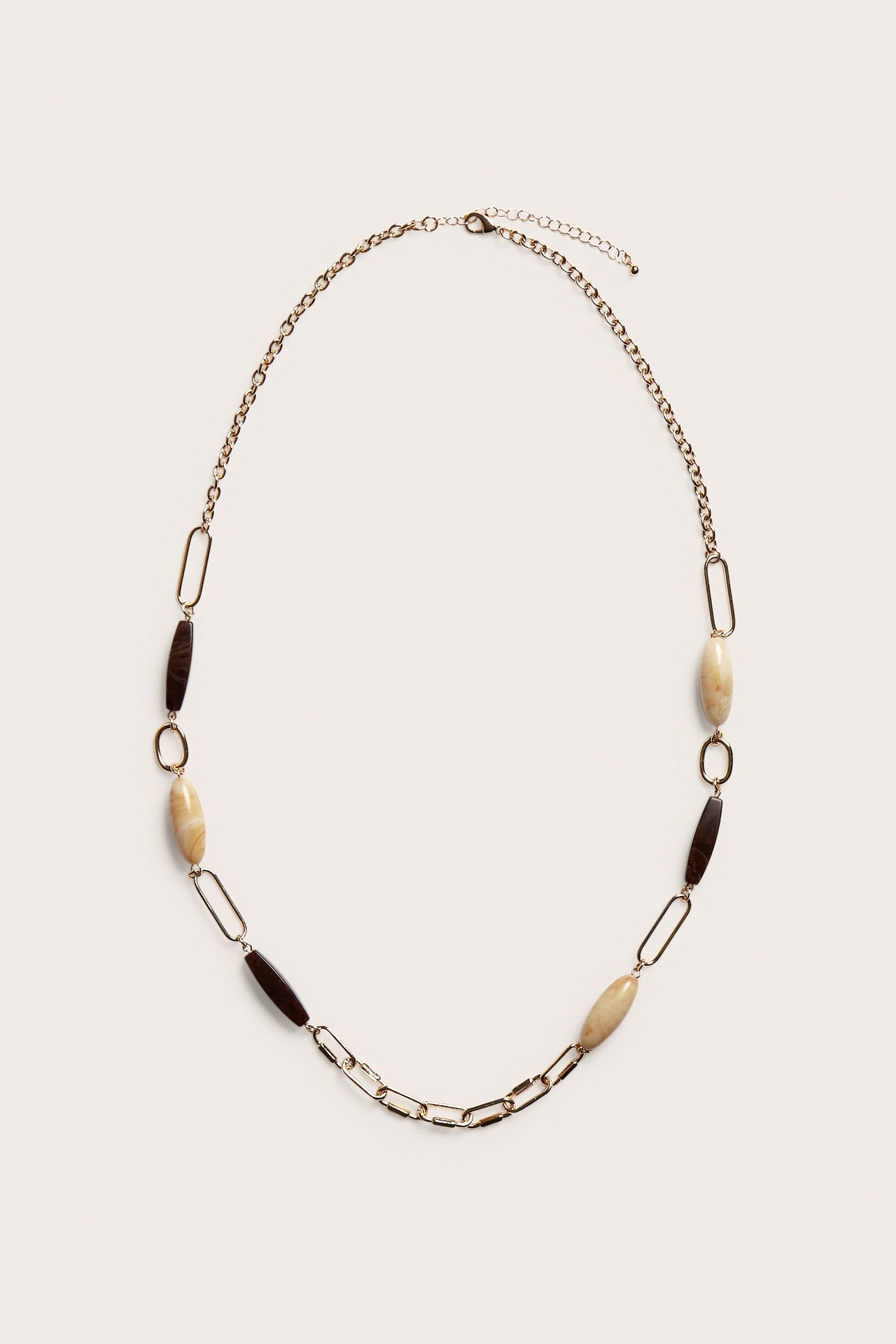 Ylhäältä näkymä: Kultainen kaulakoru vaaleanbeigeillä ja tummanruskeilla muovikivillä, sekä sekaketjulinkeillä.