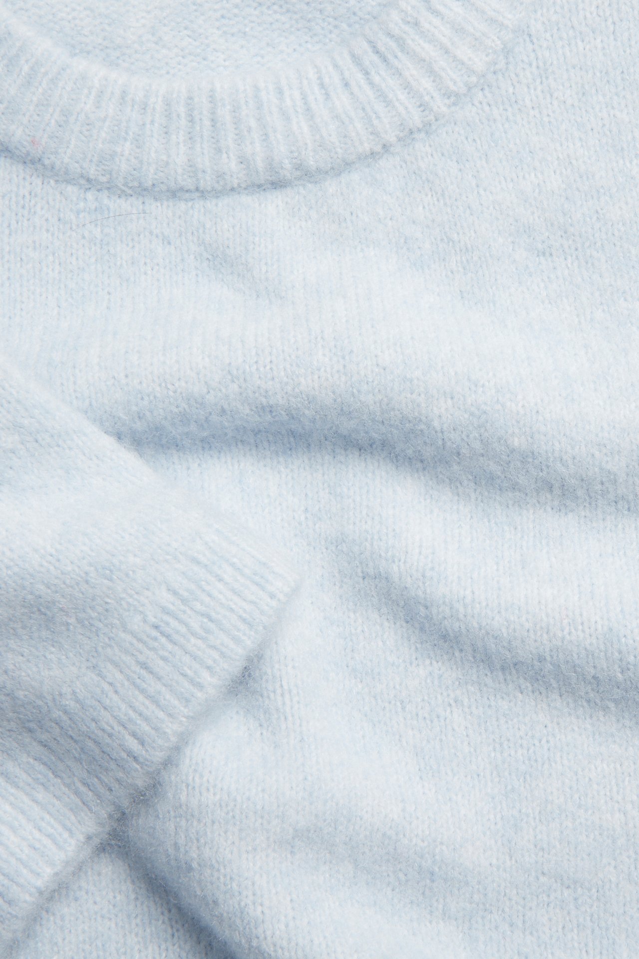 Lähikuva vaaleansinisestä hienoneulepaidasta, jossa pehmeä pinta, resori pääntie ja hiha.