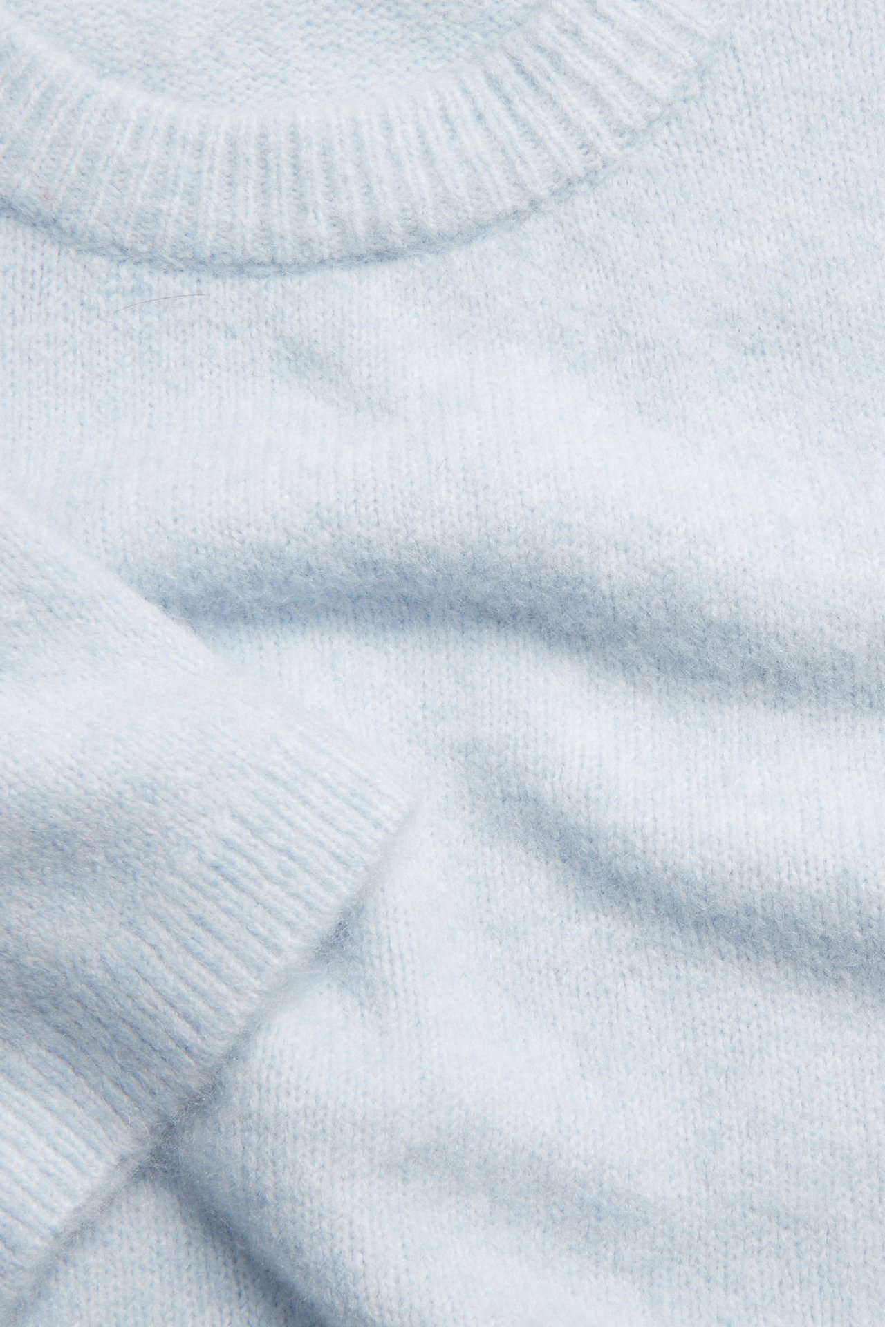 Zbliżenie: jasnoniebieski, cienki sweter z miękką fakturą, prążkowany dekolt, widoczny rękaw.