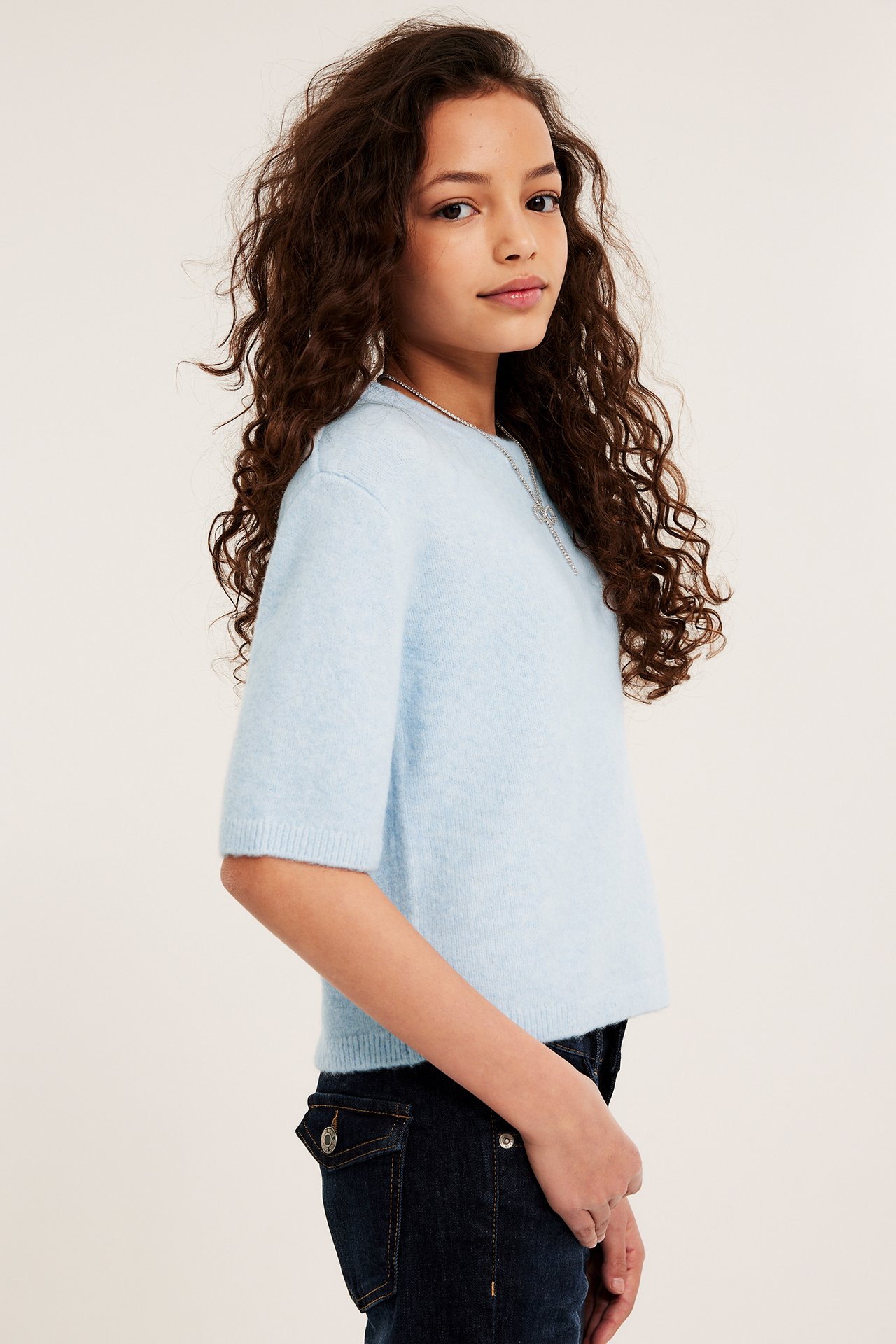 Sidestykke av barn med lys blå finstrikket T-skjorte, mørkeblå jeans og sølvkjede.