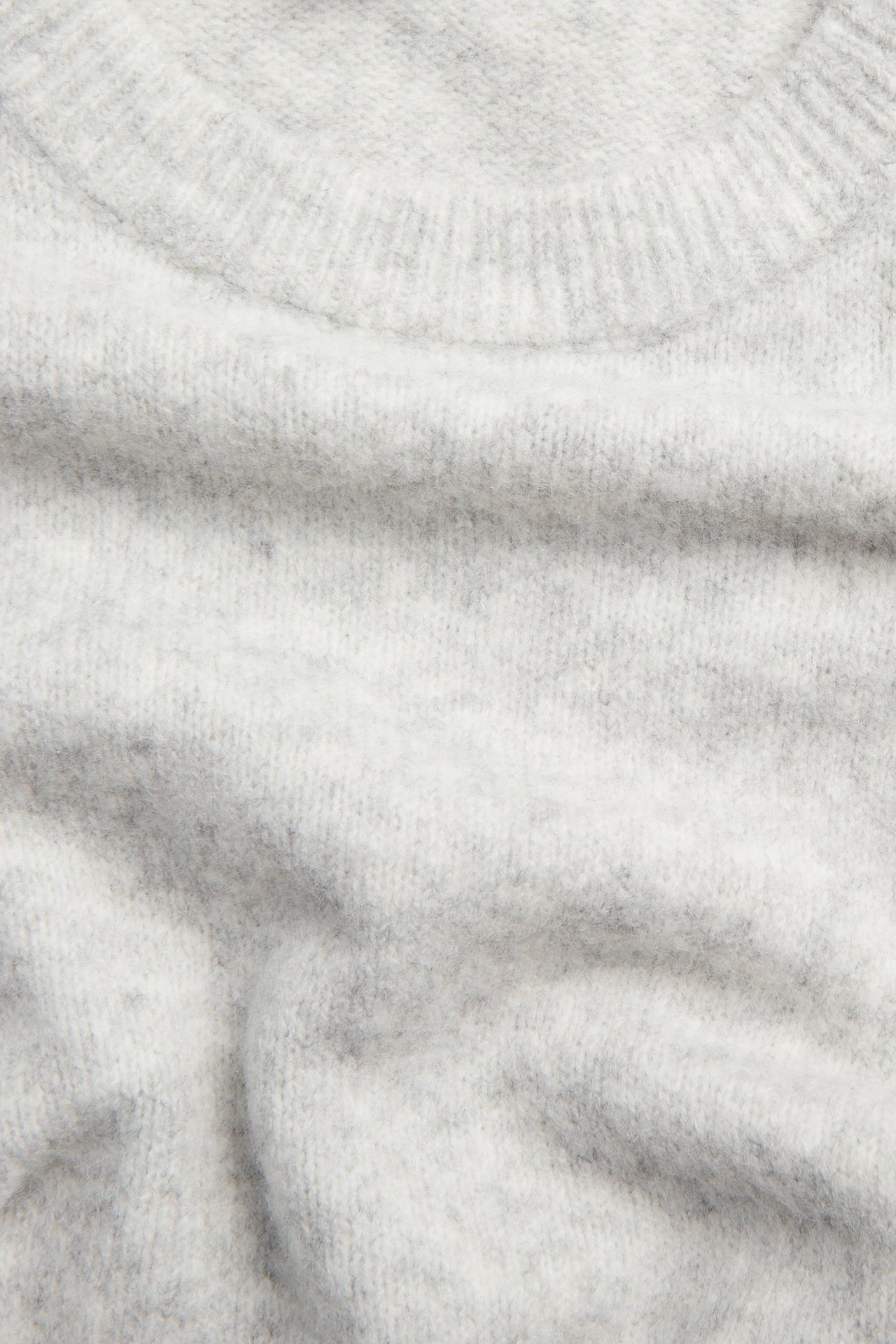 Lähikuva pehmeästä, vaaleanharmaasta meleeratusta hienoneulepaidasta ribbikauluksella.