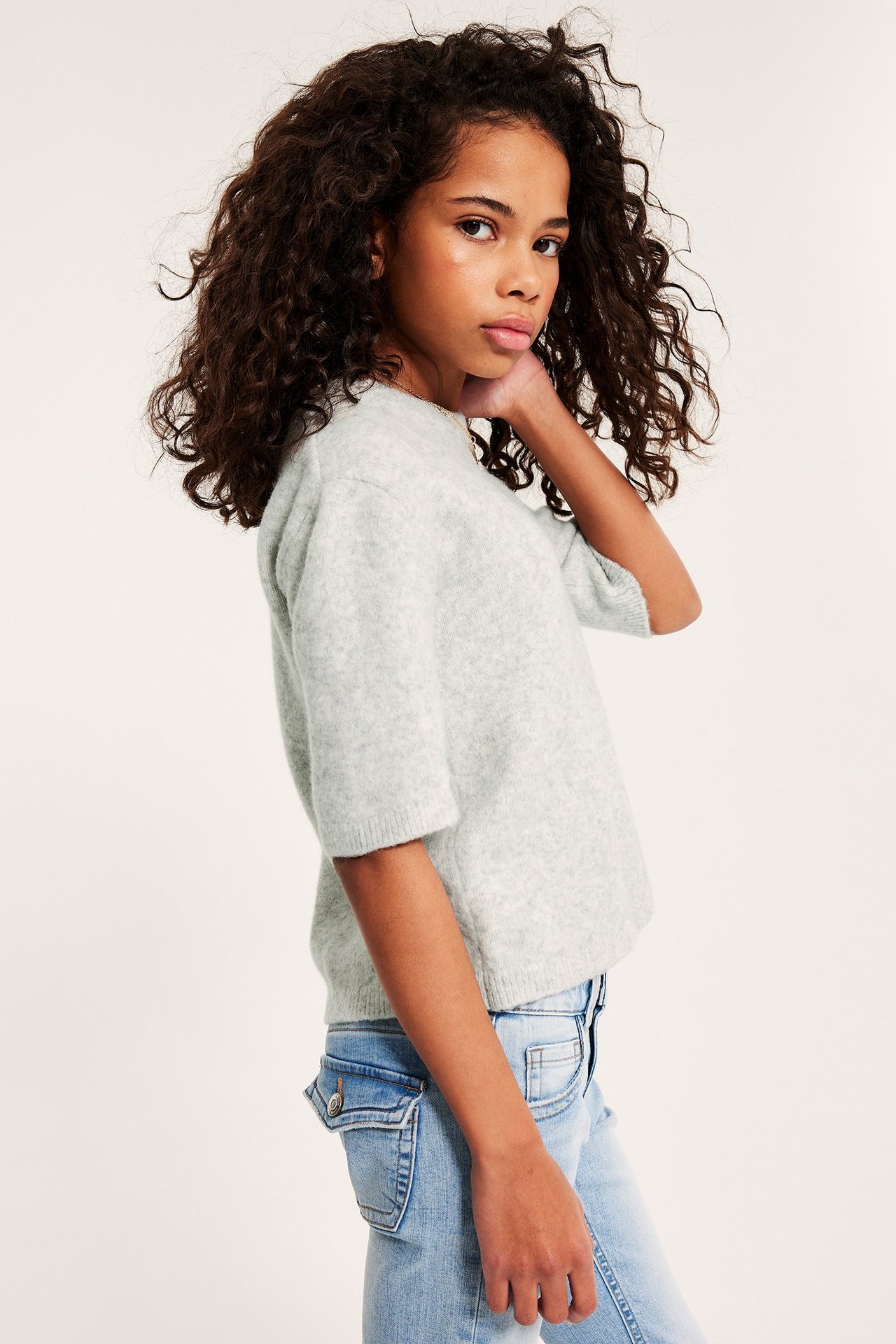 Sidebilde av et barn i en lys grå finstrikket kortermet genser og lyseblå jeans.