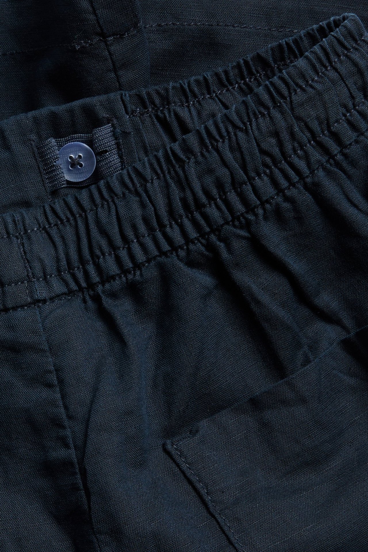 Lähikuva tummansinisistä pellavasekoiteshortseista, joissa resori vyötäröllä ja säädettävä nappi.