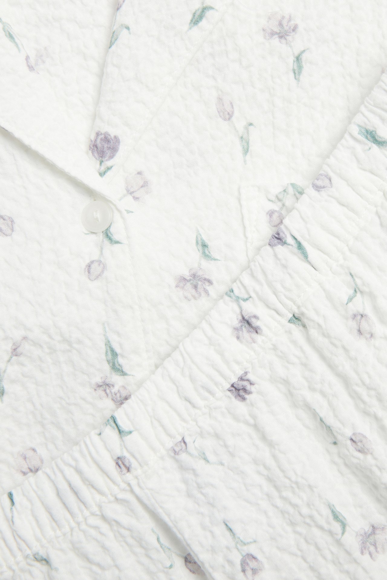 Nærbilde av et offwhite teksturert pyjamasett med blomstermønster og knapplukking.