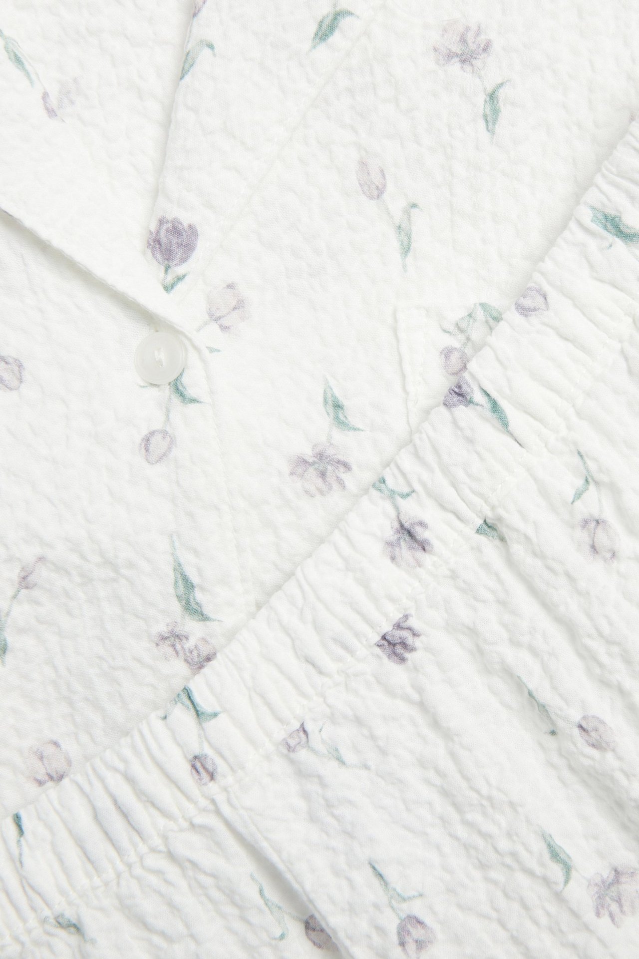 Nærbilde av et offwhite teksturert pyjamasett med blomstermønster og knapplukking.