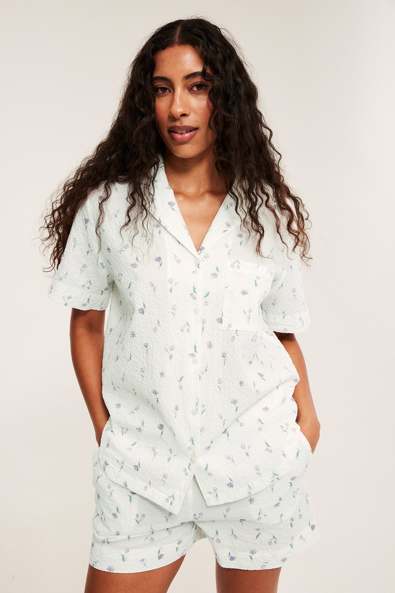 Widok z przodu: kobieta w kremowym, fakturowanym komplecie piżamowym w kwiaty, koszulka i szorty.