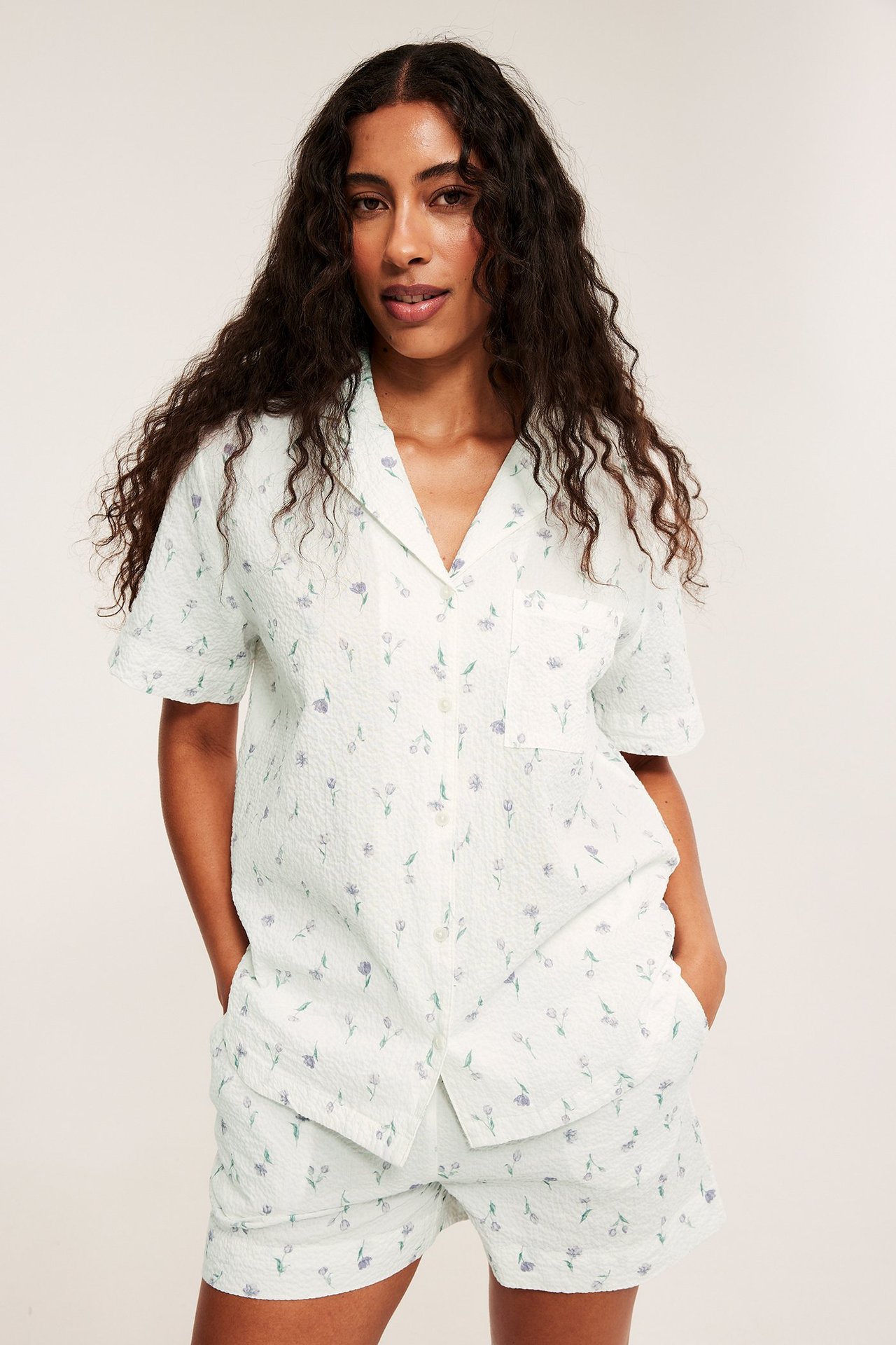 Widok z przodu: kobieta w kremowym, fakturowanym komplecie piżamowym w kwiaty, koszulka i szorty.