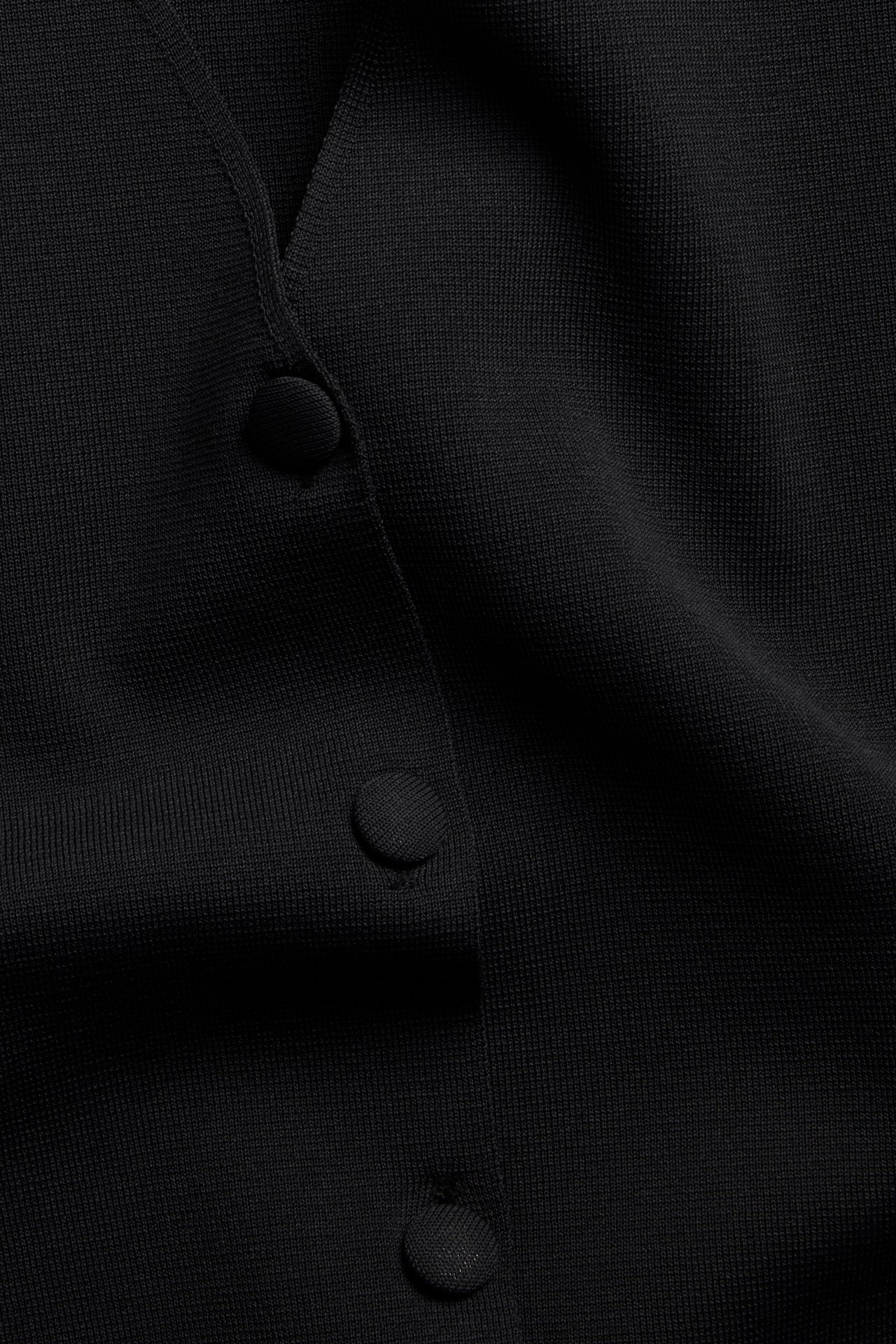 Lähikuva mustasta yksivärisestä neuletakista, jossa kolme kangaspäällysteistä nappia edessä.