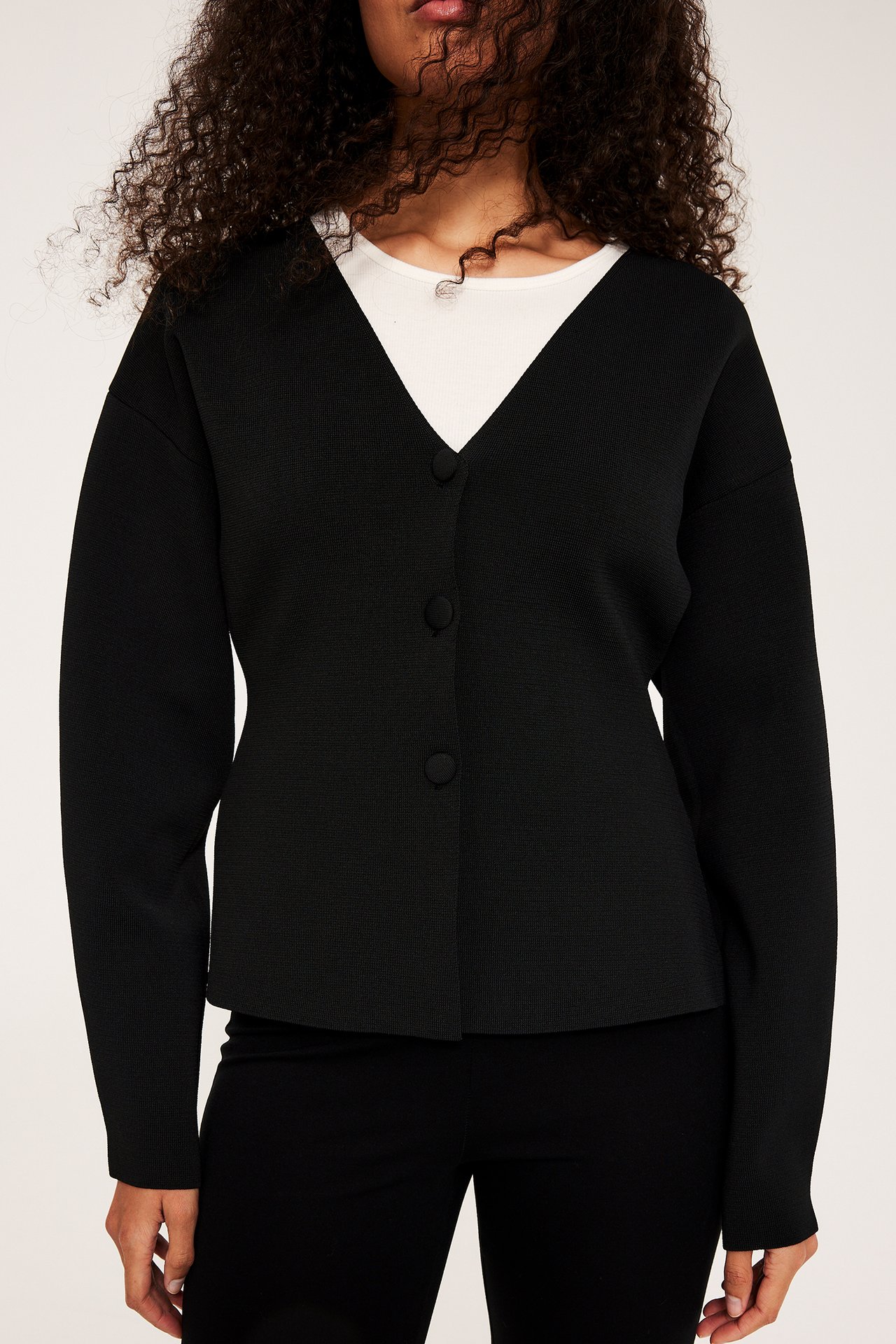 Svart damecardigan med V-hals og tre knapper, brukt over hvit topp og svarte bukser.
