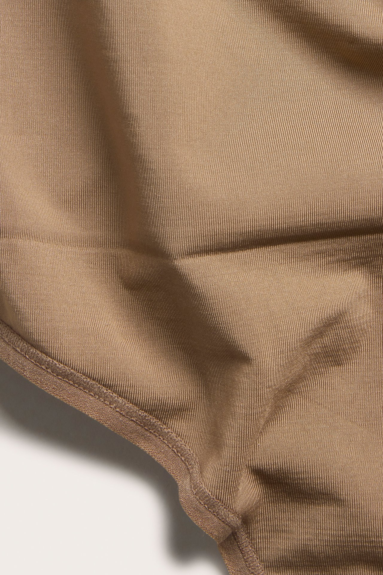 Lähikuva yksivärisestä ruskeasta ribatusta string-pikkuhoususta kierrätyspolyesteristä.