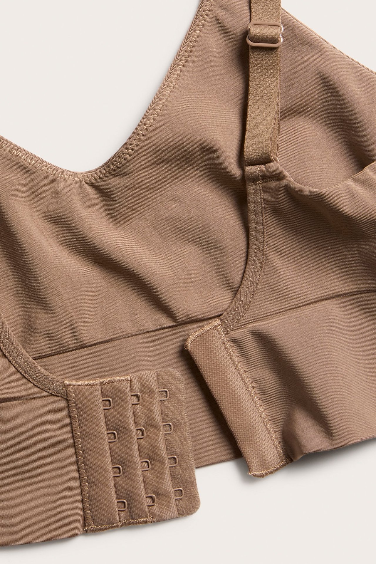 Vinklad närbild av en brun sömlös mjuk-bh med justerbara axelband och 4x3 hak- och hyskknäppning.