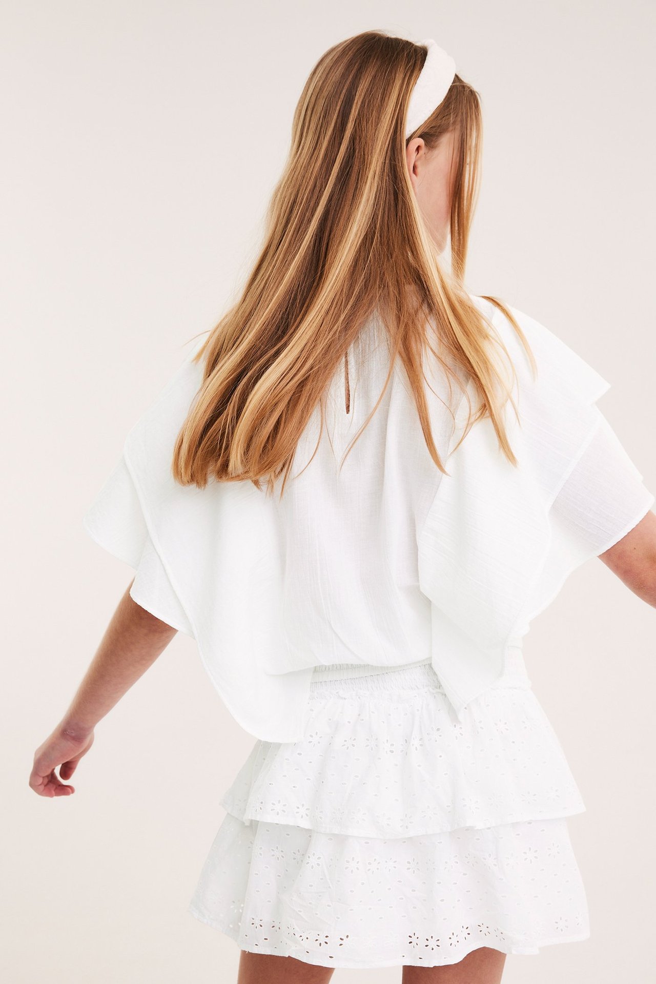 Widok z tyłu: dziecko w białej bluzce z rękawami nietoperzowymi, smockiem, białej spódnicy z haftem, opasce.