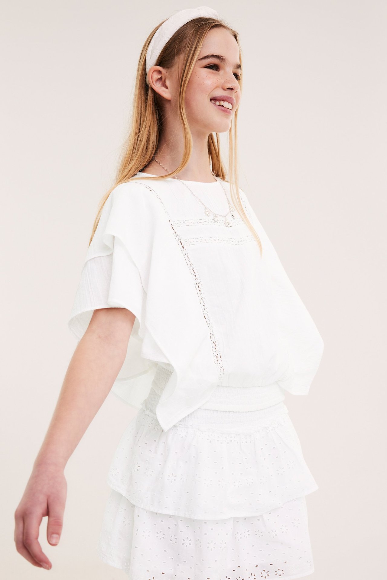 Dziecko w białej bawełnianej bluzce nietoperzowej z koronką, marszczoną talią, spódnicą i opaską.
