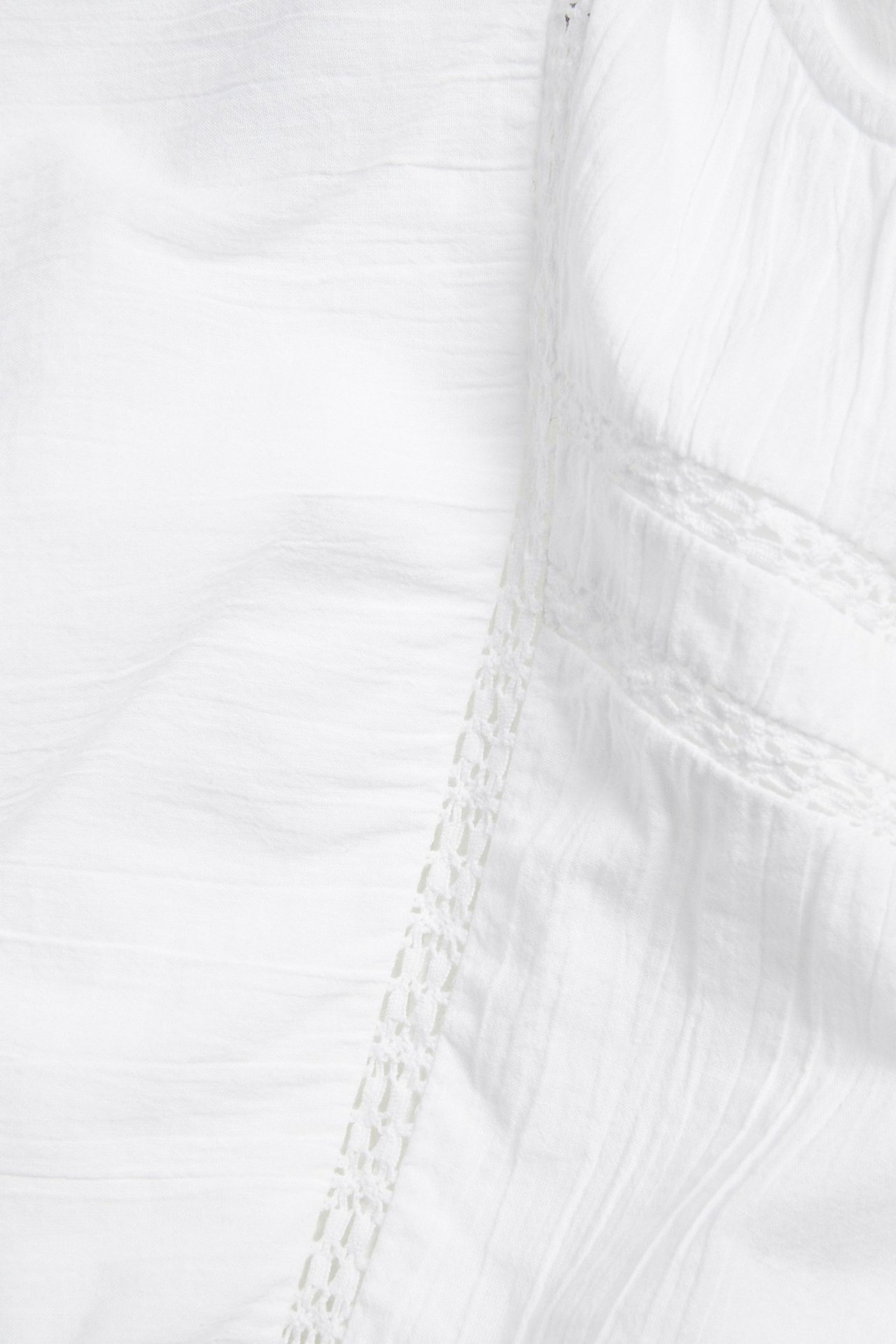 Närbild av vit skrynklig bomullsblus med delikata spetsdetaljer.