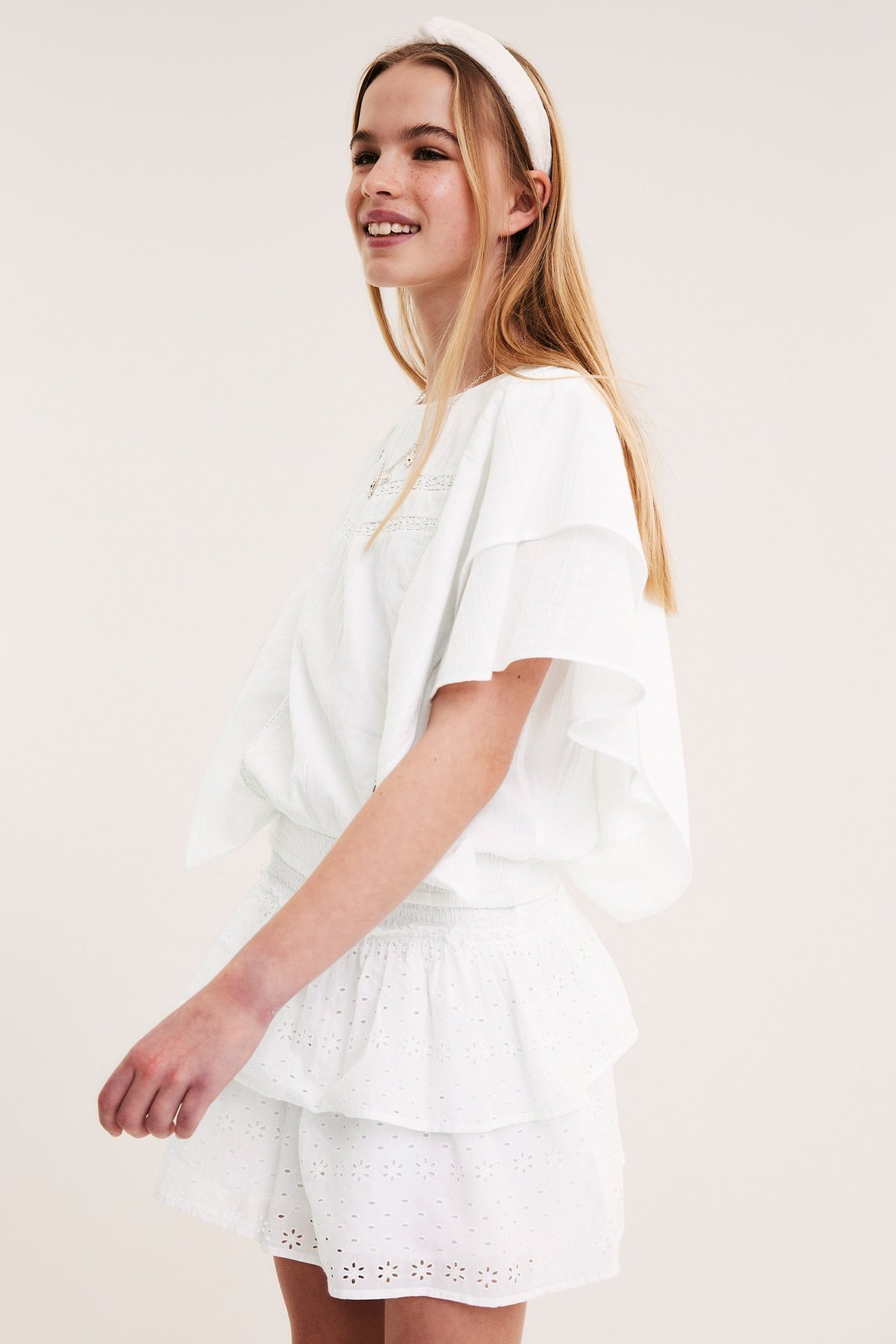 Vit bomullsblus med spetsdetaljer, smock i midjan, på tjej i frontvy.