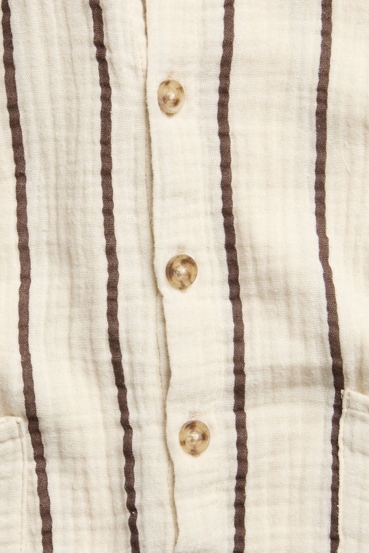 Zbliżenie: beżowy, pasiasty bawełniany pajac niemowlęcy z guzikami z przodu i widoczną kieszenią.