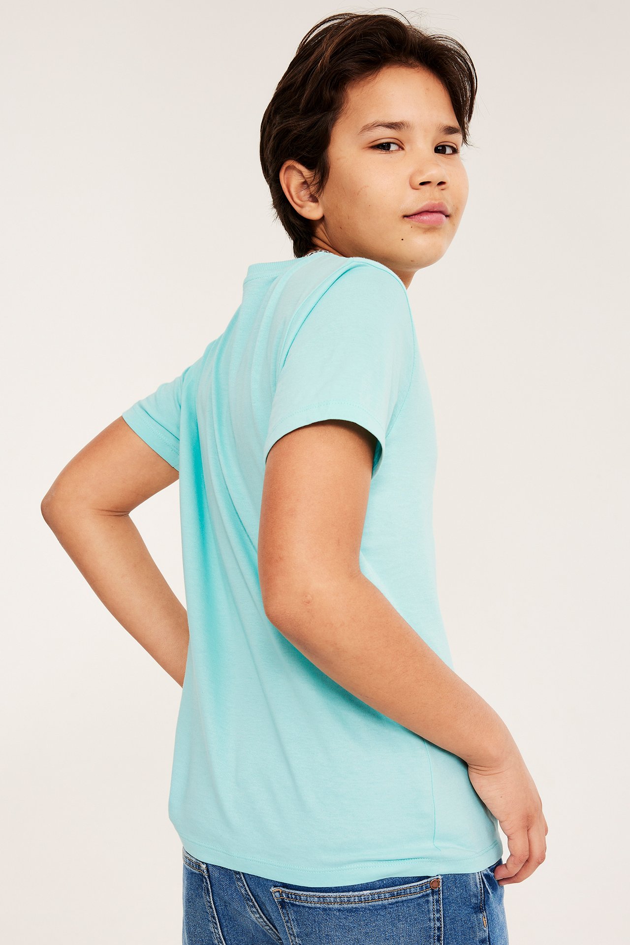 Sivukuva pojasta yllään vaalean turkoosi puuvillainen t-paita ribbineulekauluksella ja siniset farkut.