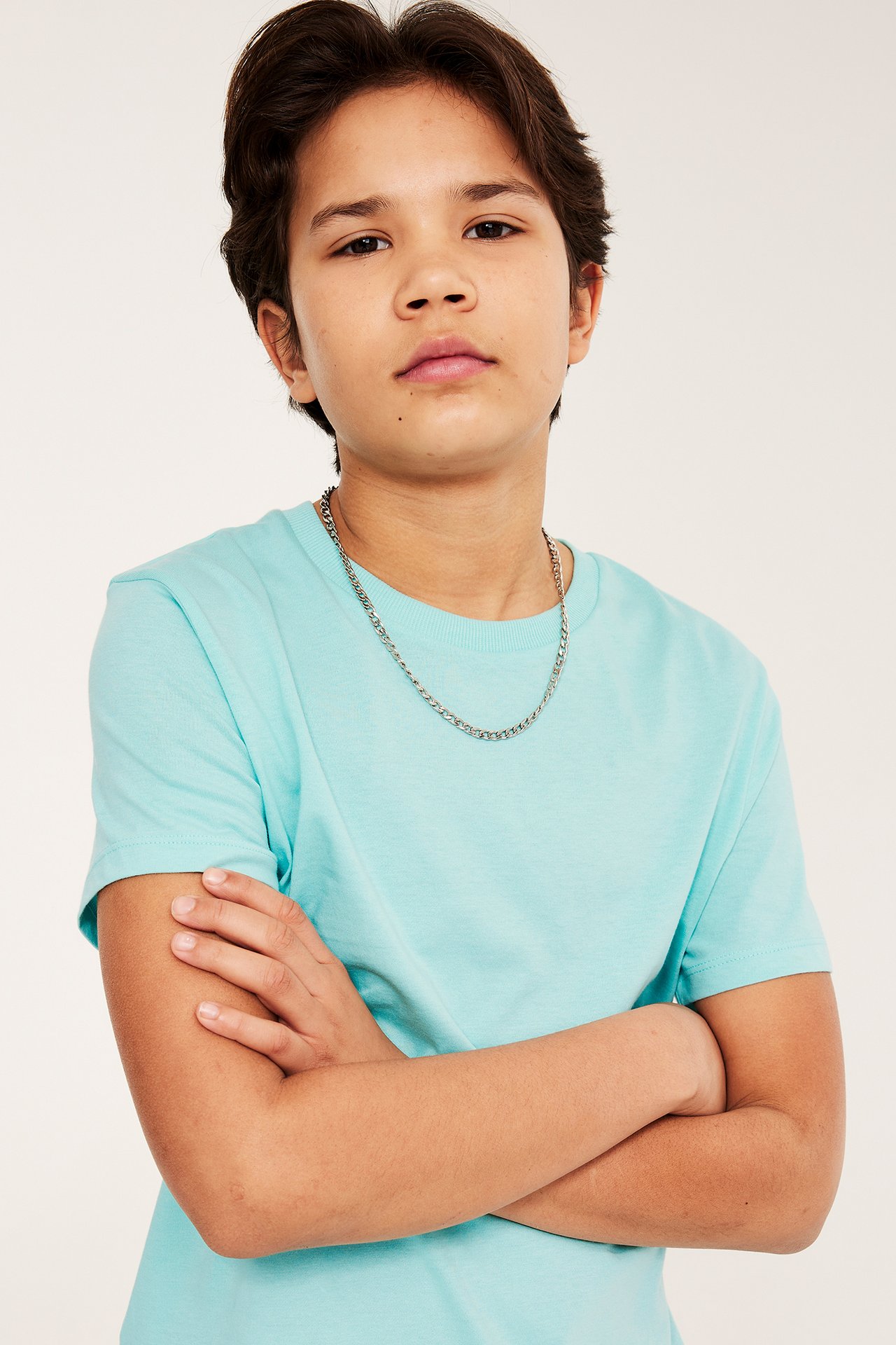 Edestä: Lapsi vaaleanturkoosissa puuvilla-T-paidassa ribbineulekauluksella ja hopeaketjulla.