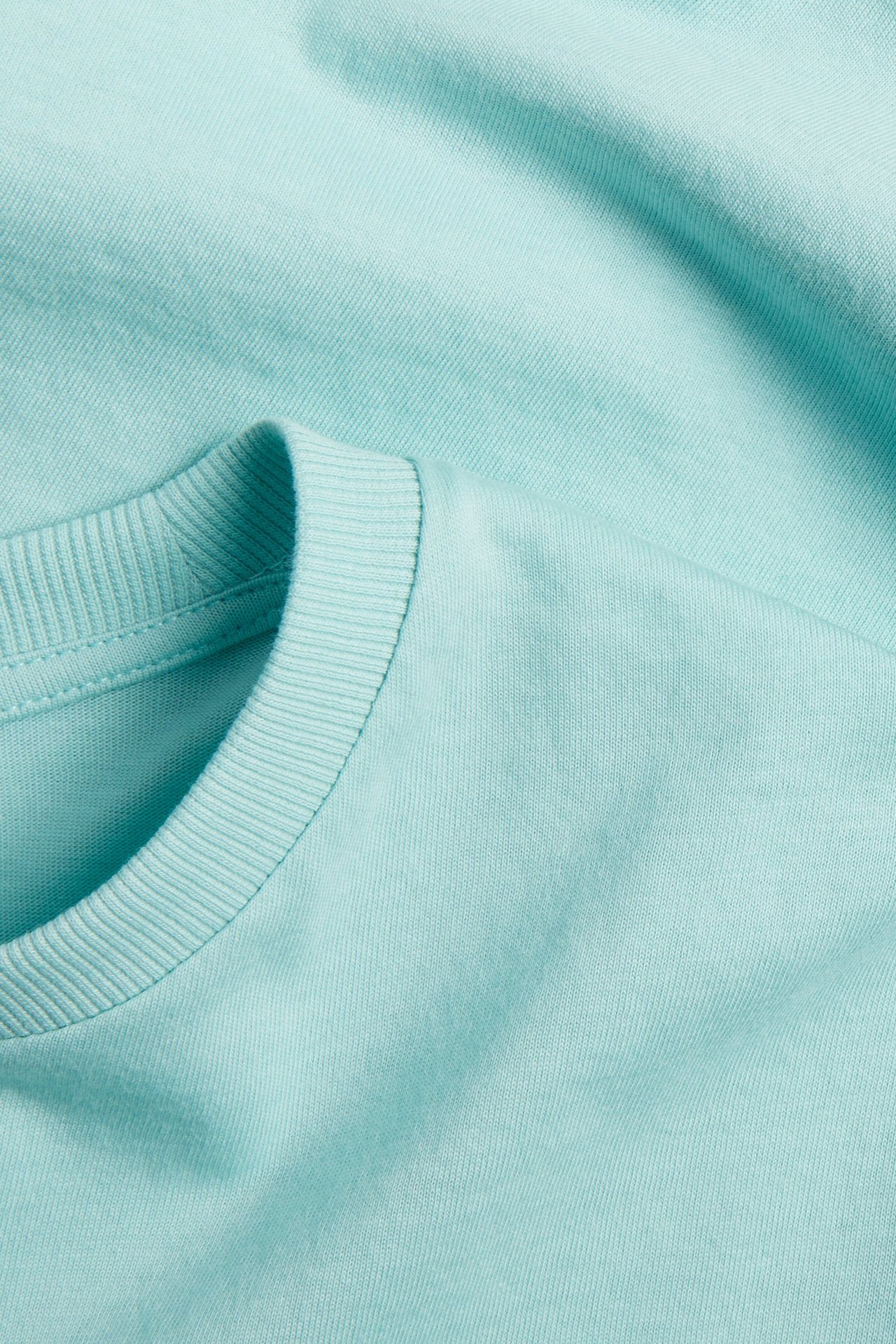 Zbliżenie jasnoturkusowej, jednokolorowej bawełnianej koszulki z prążkowanym okrągłym dekoltem.