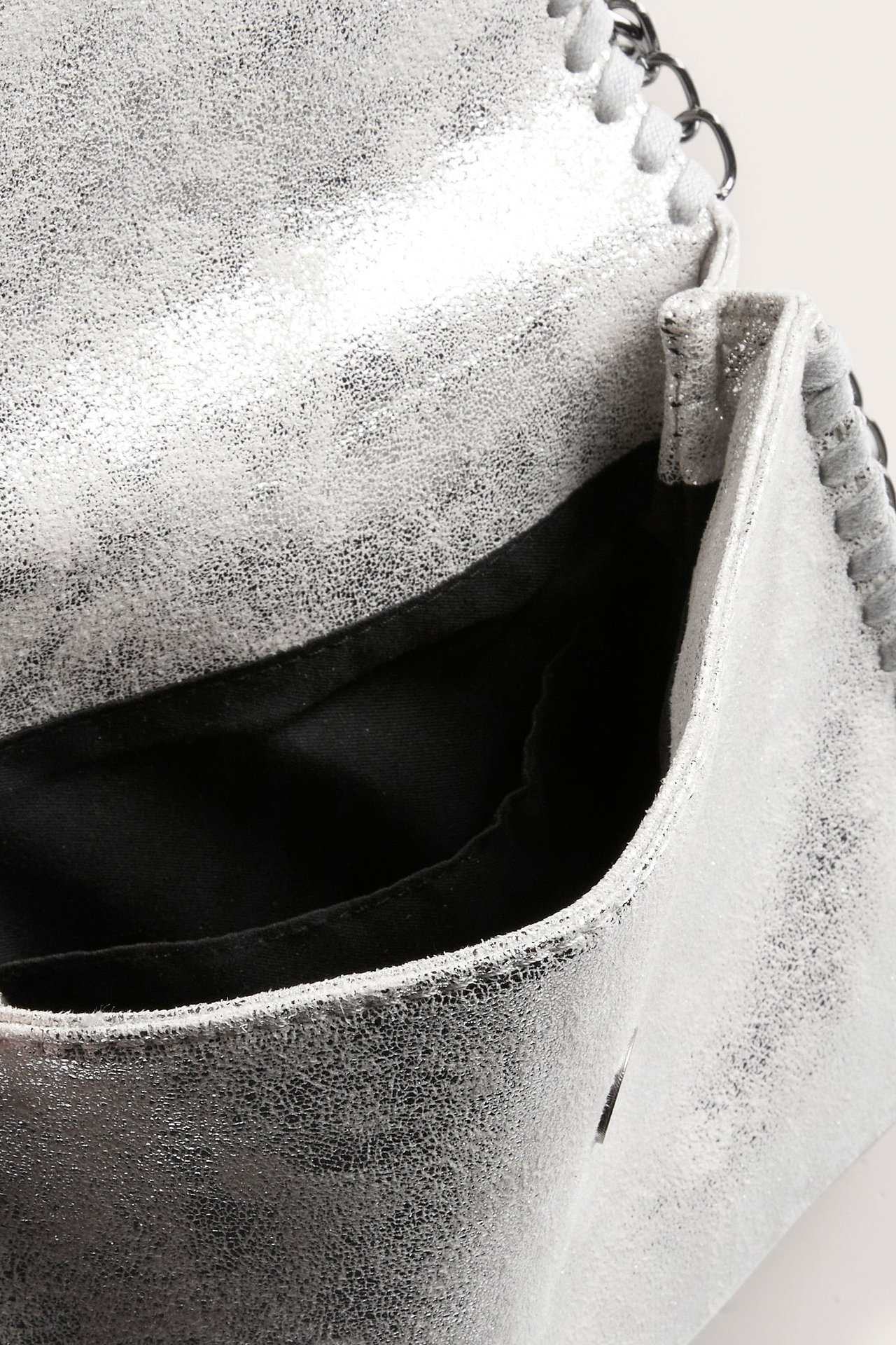 Lähikuva hopeisesta kuvioidusta käsilaukusta, jossa läppä, musta sisus ja metalliketjukoriste.